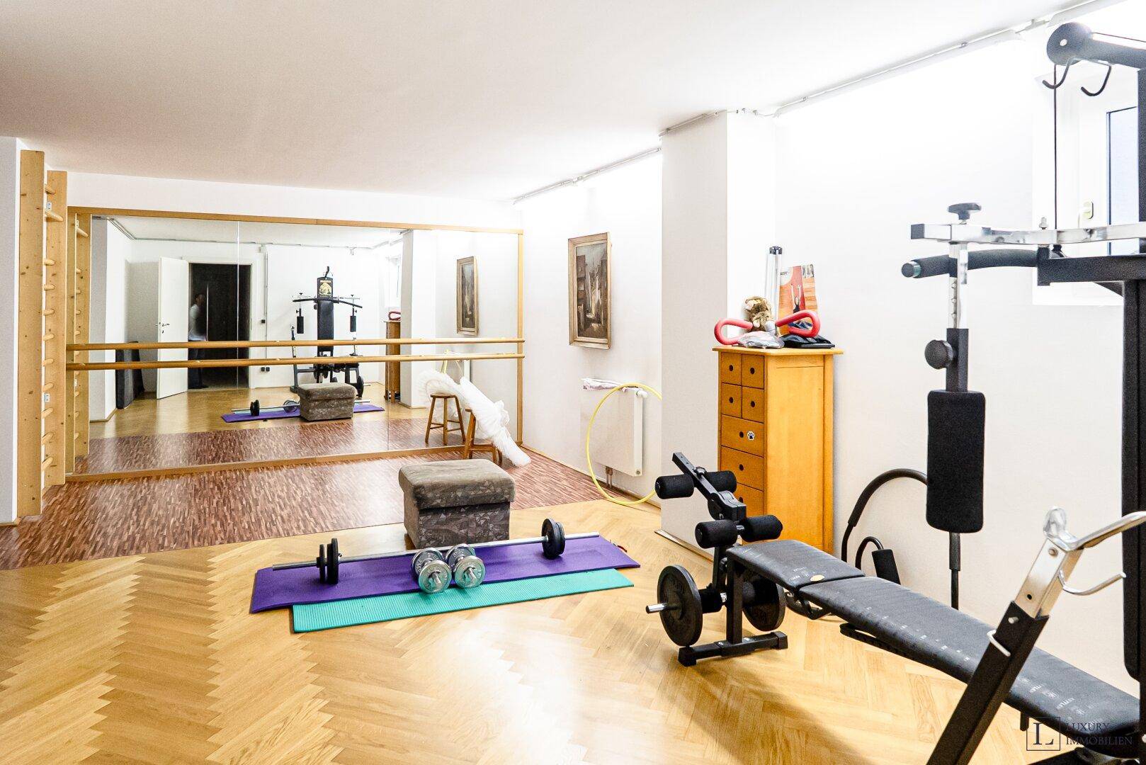 Geräumiger Fitnessraum mit Spiegelwand, Ballettstange und verschiedenen Trainingsgeräten.