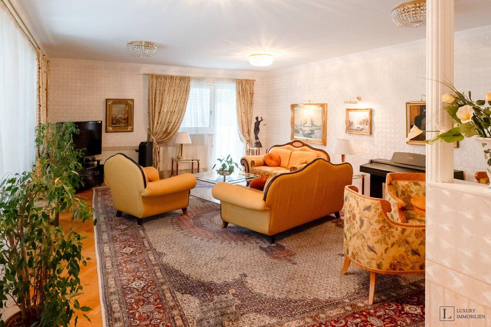 Großzügiges Wohnzimmer mit bequemen Sitzgelegenheiten, Teppich und Blick ins Grüne.