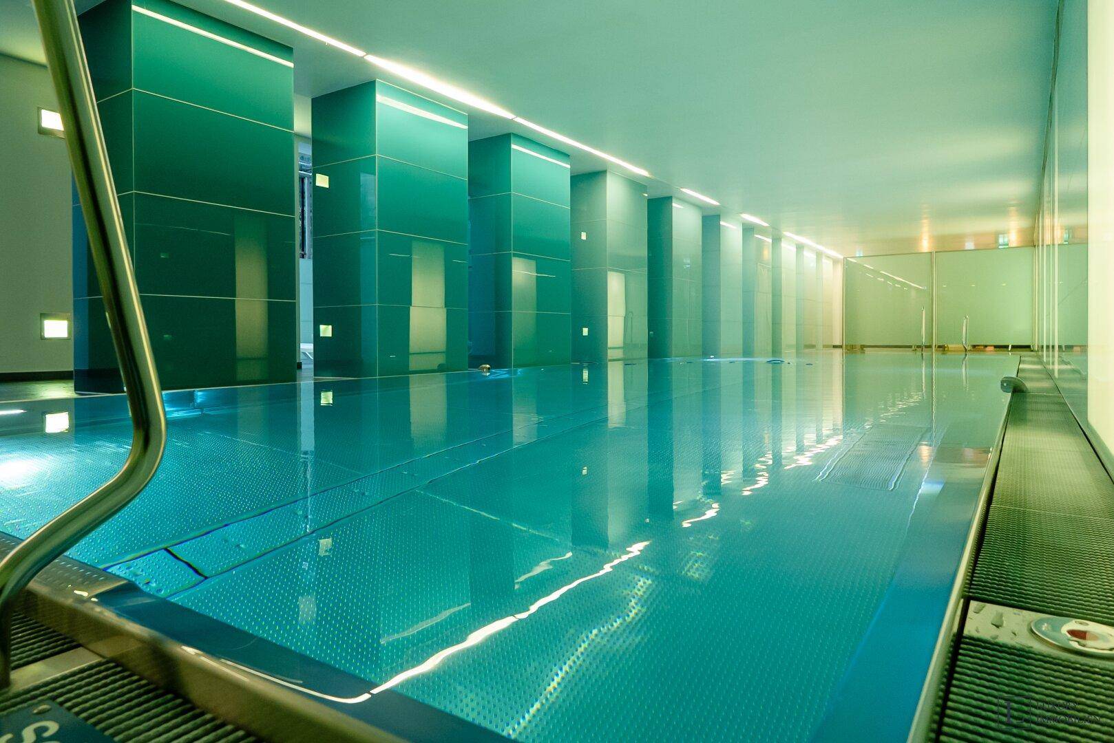 Modernes Hallenbad mit türkisfarbenem Wasser und beleuchteten Säulen, ideal zum Schwimmen.