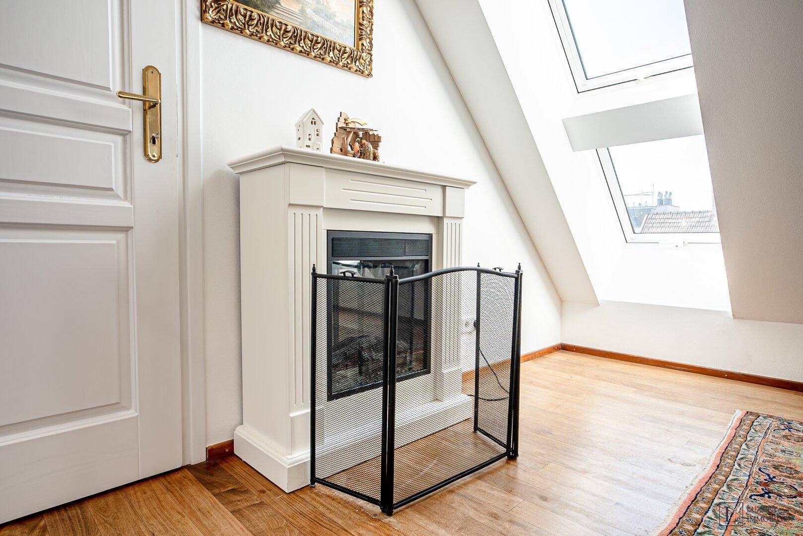 Gemütlicher Dachraum mit Kamin, Holzparkettboden und Dachfenstern für natürliches Licht.