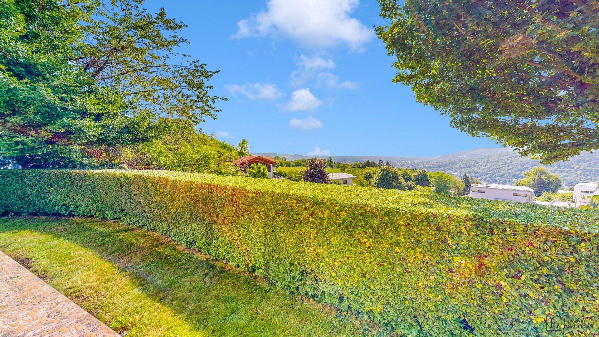 Gepflegte Hecke im Gartenbereich mit weitem Blick auf die grüne Landschaft und die umliegenden Hügel.