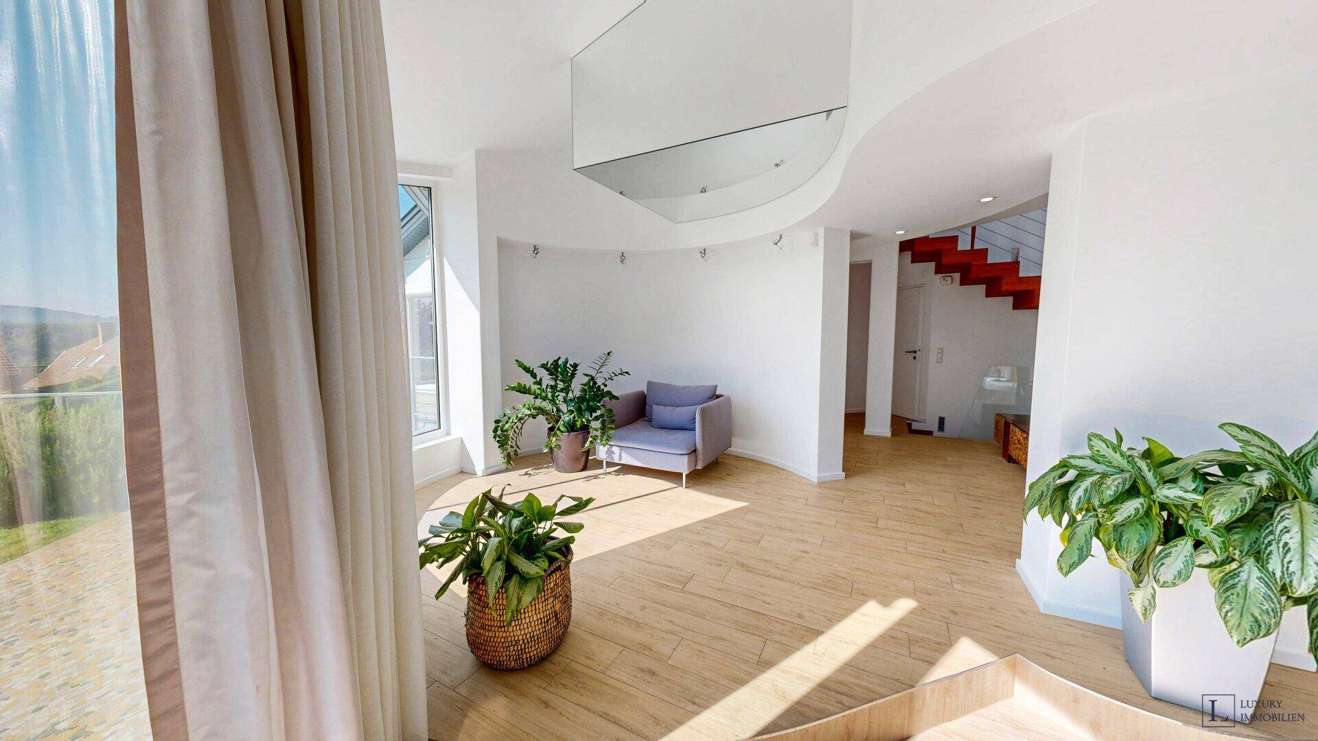 Heller Eingangsbereich mit geschwungenen Wänden, Pflanzen und einer modernen Treppe im Hintergrund.