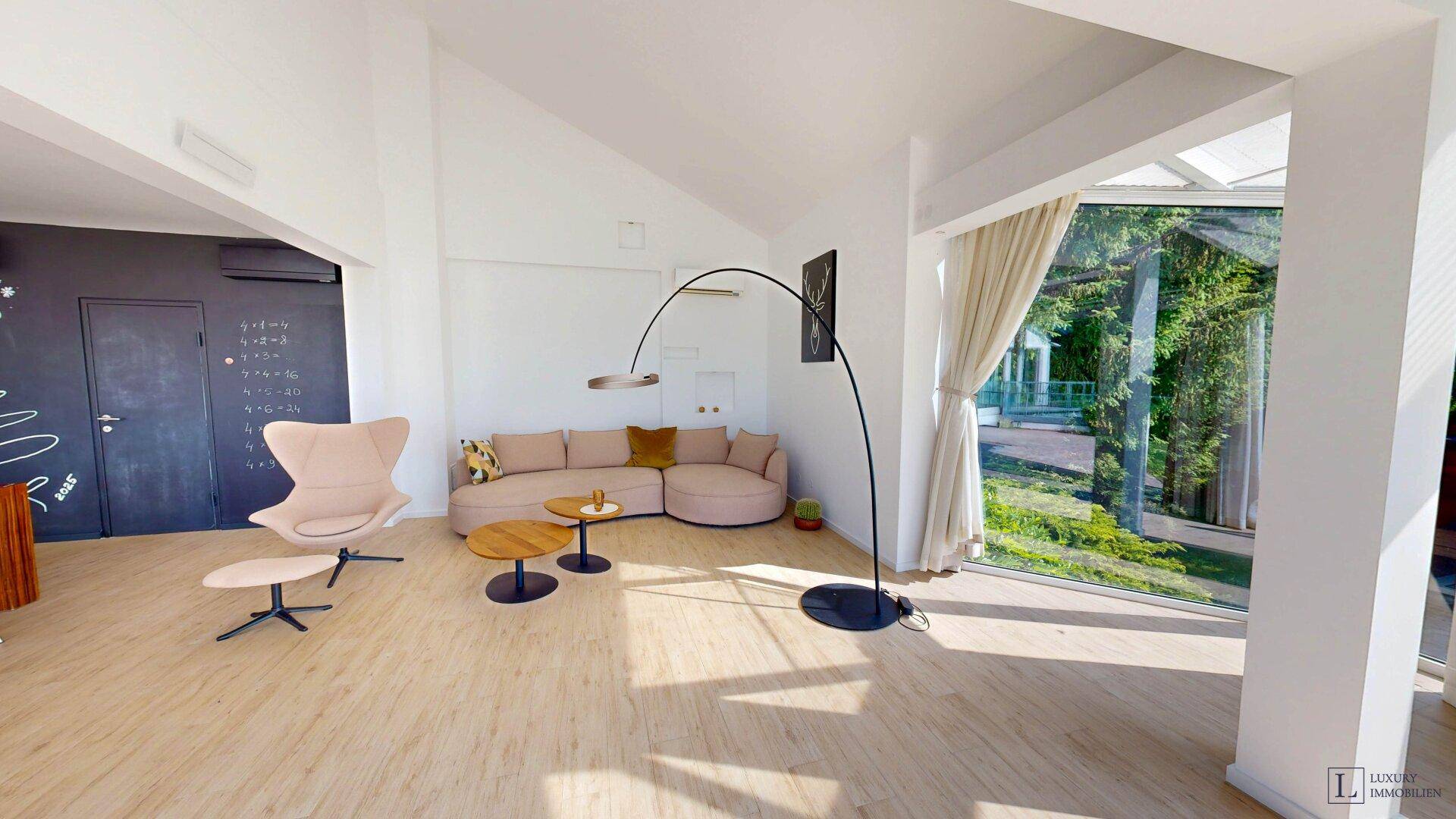Modern eingerichtetes Wohnzimmer mit beigem Sofa, Holzboden und großen Fenstern zum Garten.