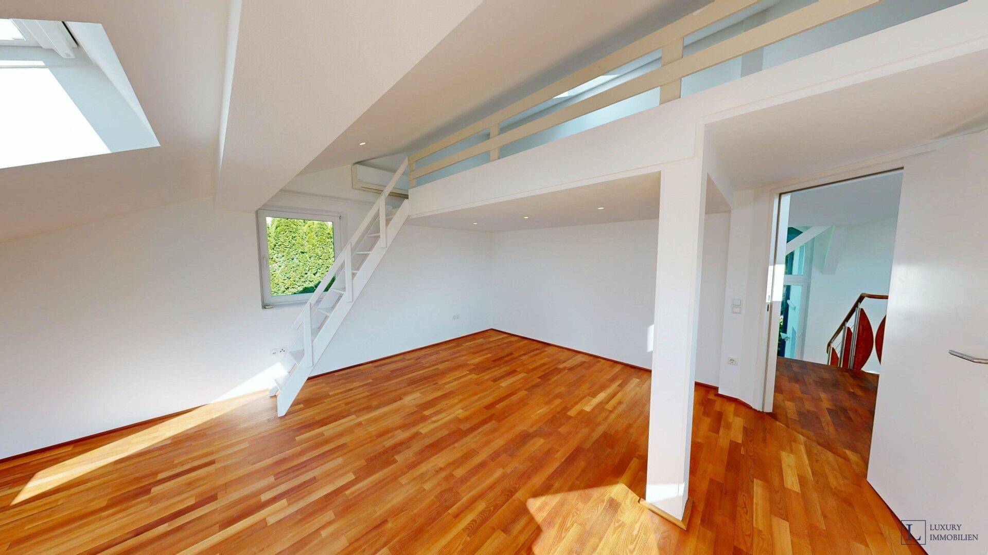 Helles Zimmer mit Holzboden, Dachschräge und einem Fenster mit Blick ins Grüne.