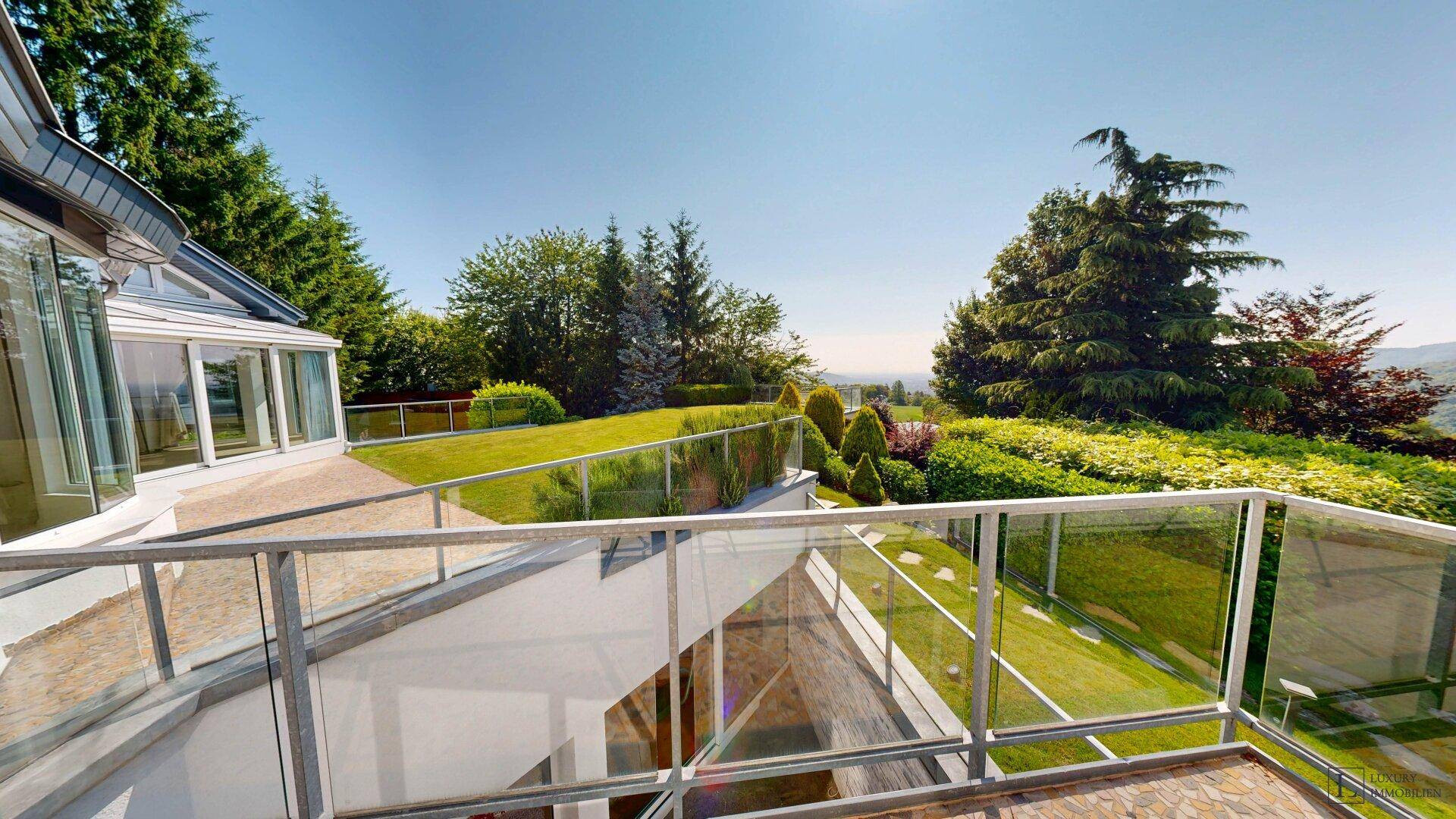 Moderne Terrasse mit Glasgeländer und weitem Blick über die hügelige Landschaft und das Anwesen.