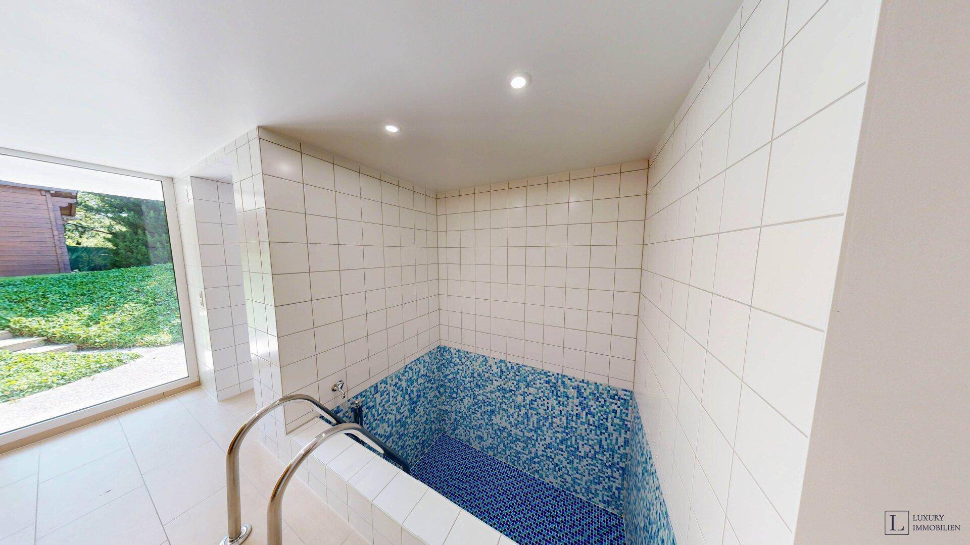 Kleiner, gefliester Whirlpool-Bereich mit blauen Mosaikfliesen und großen Fenstern zum Garten.