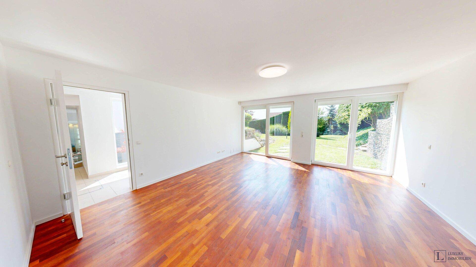 Geräumiger, heller Raum mit Holzboden und großen Schiebetüren, die Zugang zum Garten ermöglichen.