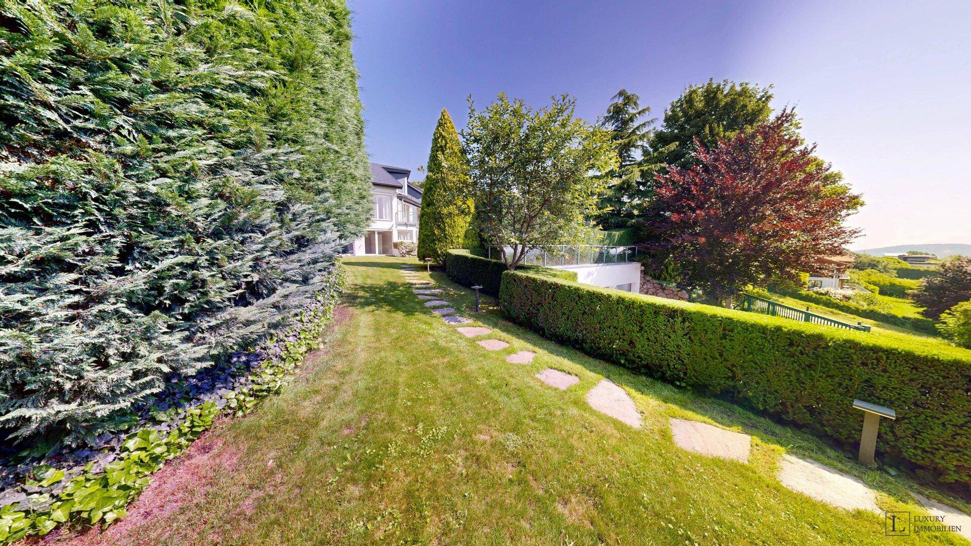 Geschwungener Gartenweg aus Trittsteinen, umgeben von hohen Hecken und Bäumen.