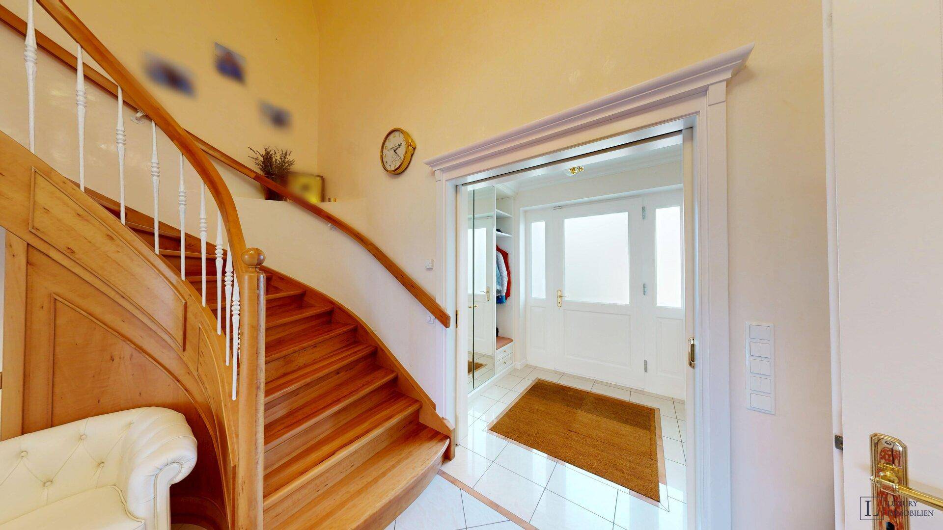 Heller Eingangsbereich mit geschwungener Holztreppe und Zugang zu weiteren Räumen.