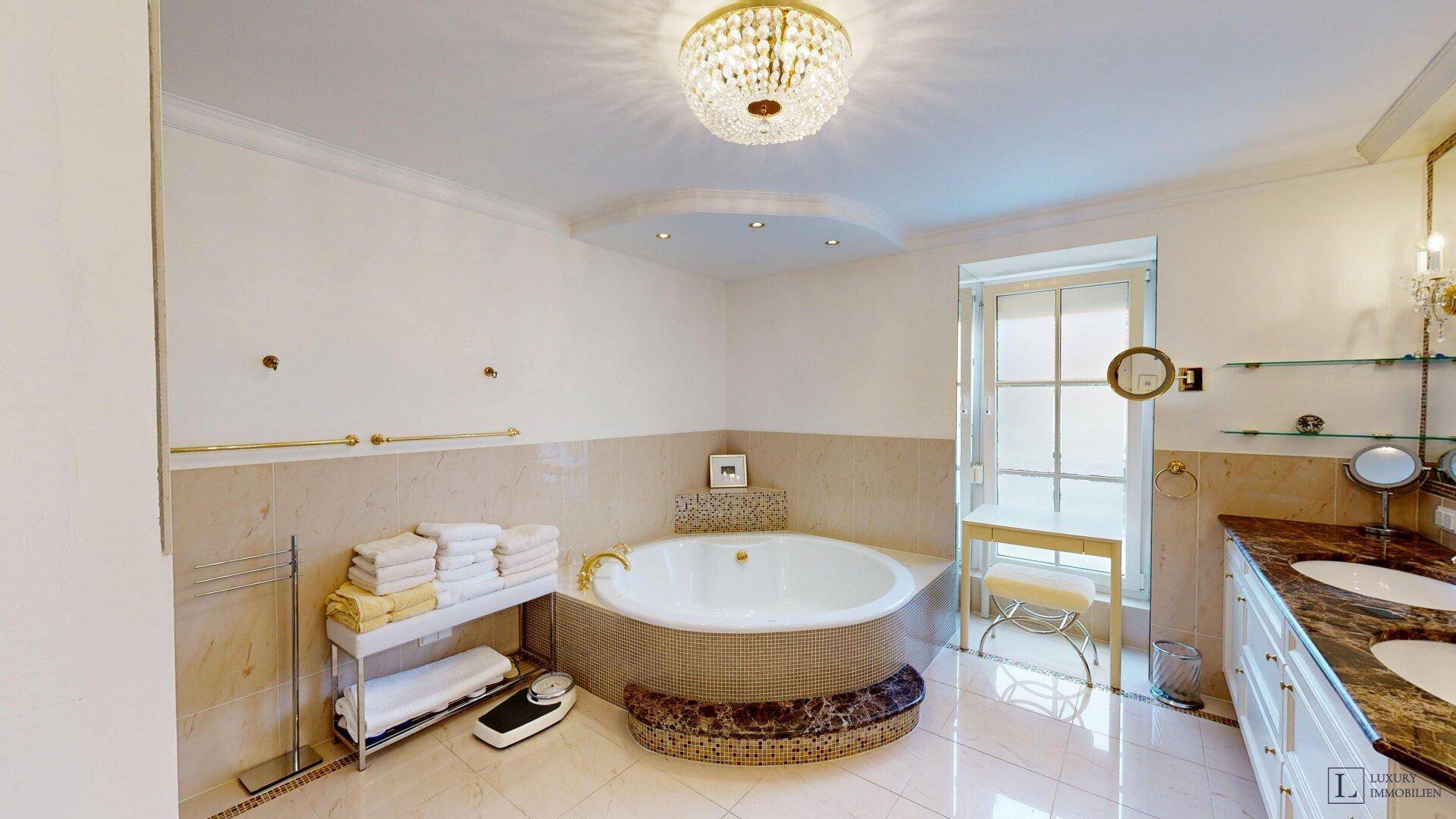 Luxuriöses Badezimmer mit runder Badewanne, Doppelwaschbecken und elegantem Kronleuchter.