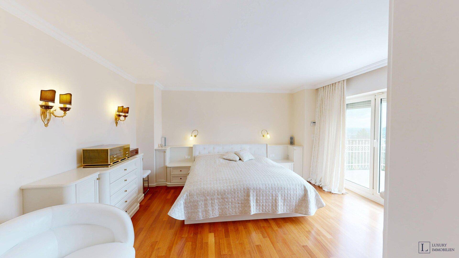 Helles Schlafzimmer mit Holzboden, weißem Mobiliar und Zugang zu einem Balkon.