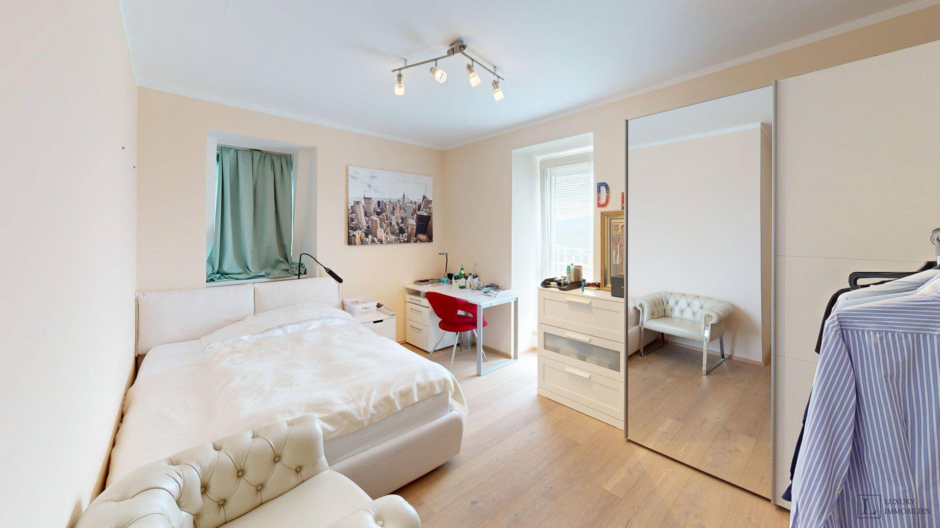Helles Schlafzimmer mit Holzboden, Schreibtisch und großem Spiegel.