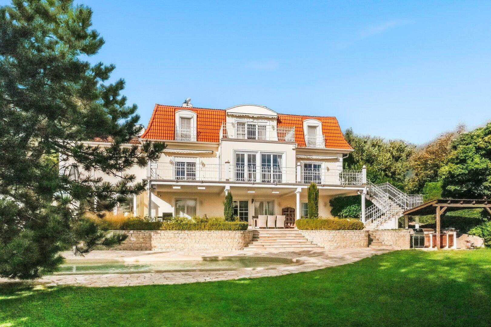 Großzügige Villa mit weitläufigem Garten, Pool und mehreren Balkonen unter blauem Himmel.