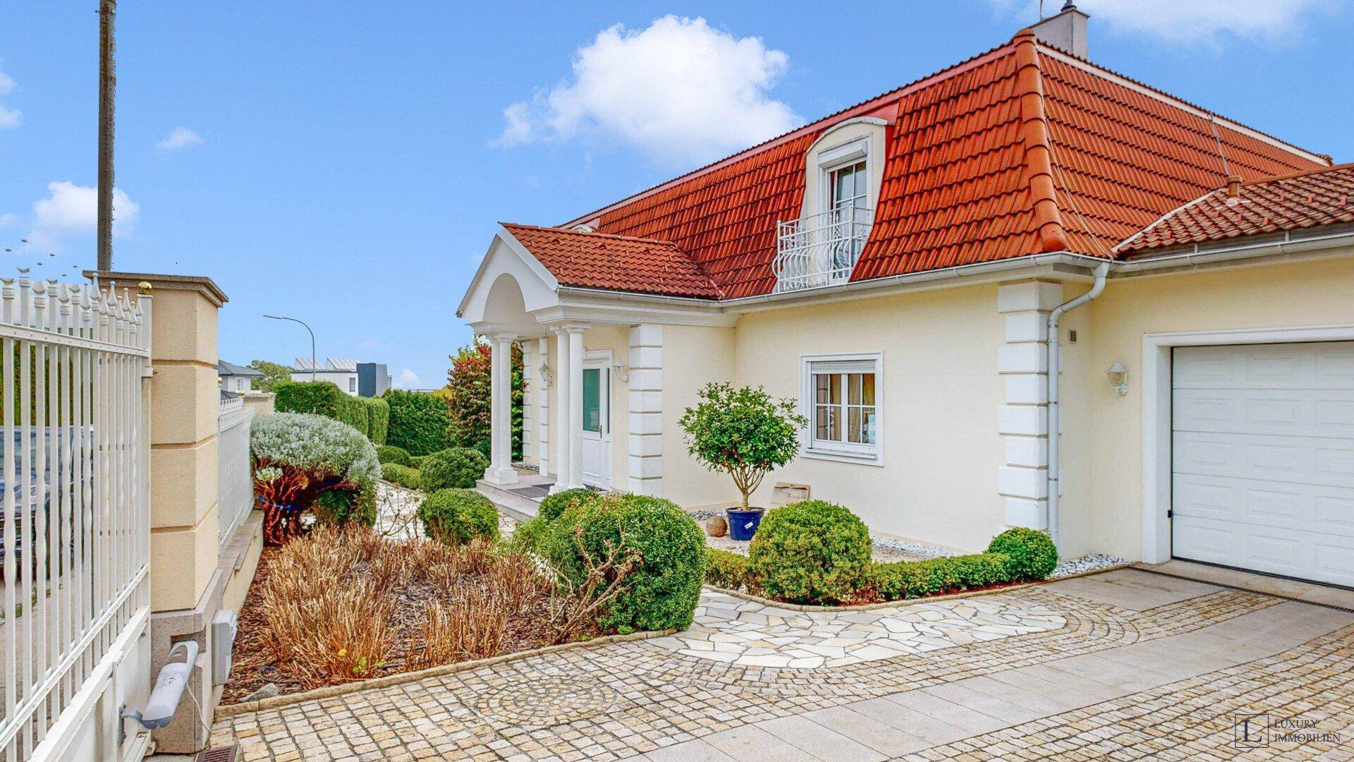 Elegante Hausfassade mit gepflasterter Auffahrt und einem schmiedeeisernen Tor.