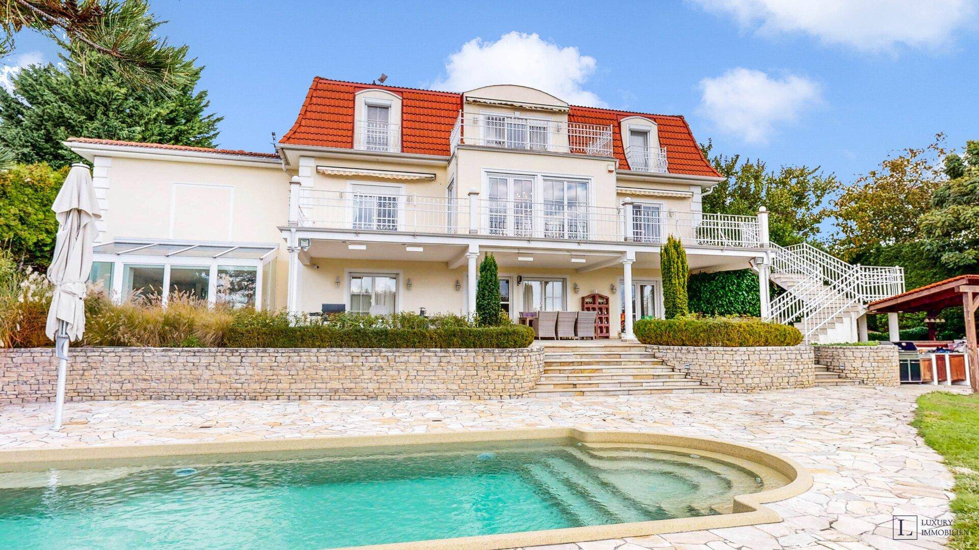Außenbereich mit großem Pool, gepflegtem Rasen und der eleganten Villa im Hintergrund.