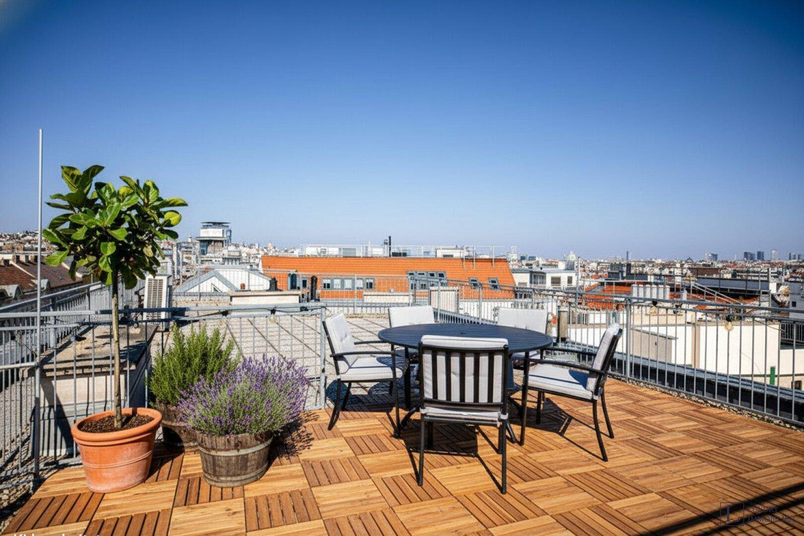 Gemütliche Dachterrasse mit Holzbodenfliesen, Esstisch und Pflanzen, mit Stadtblick.