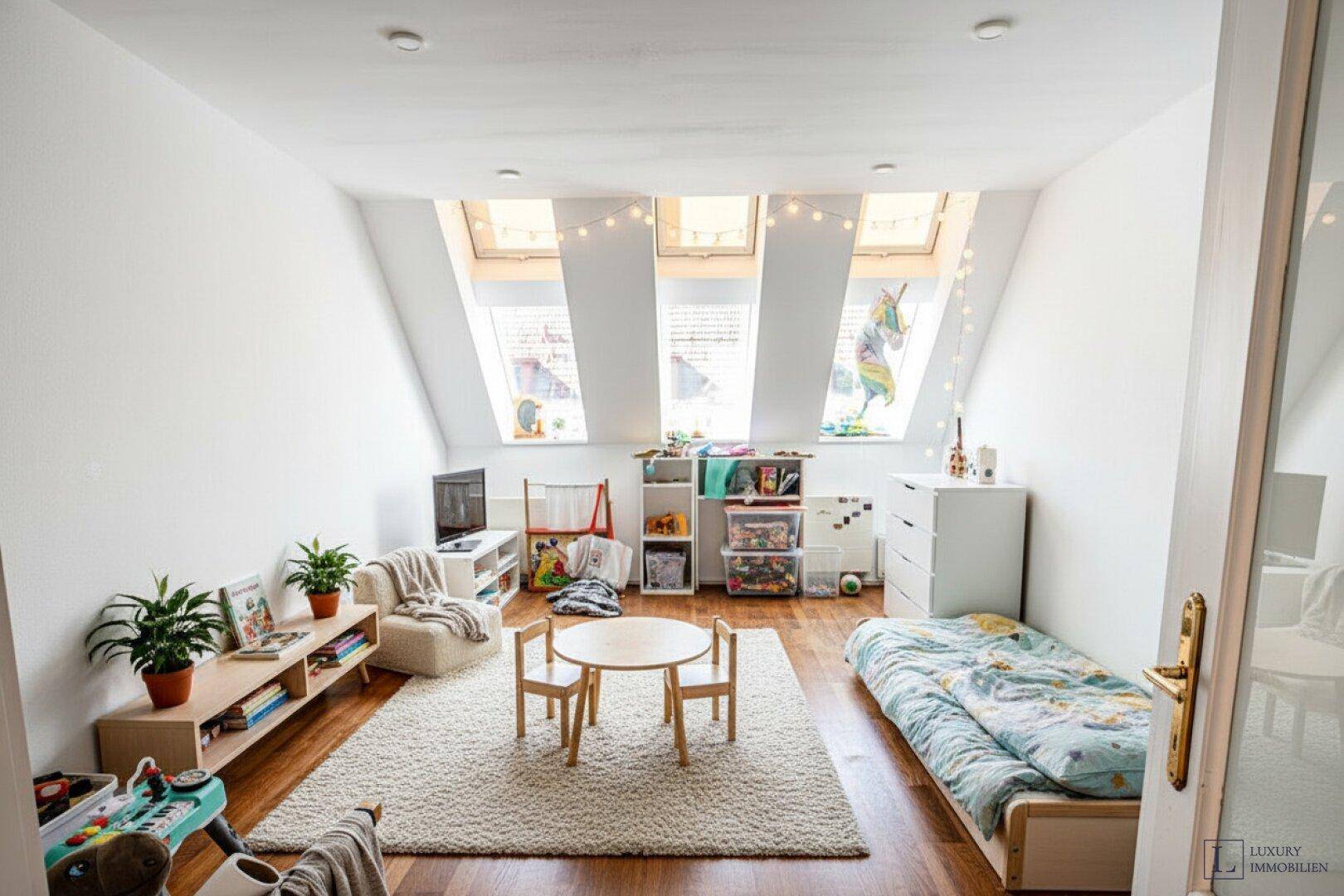 Helles Kinderzimmer mit Holzboden, Spielbereich und mehreren Dachfenstern.