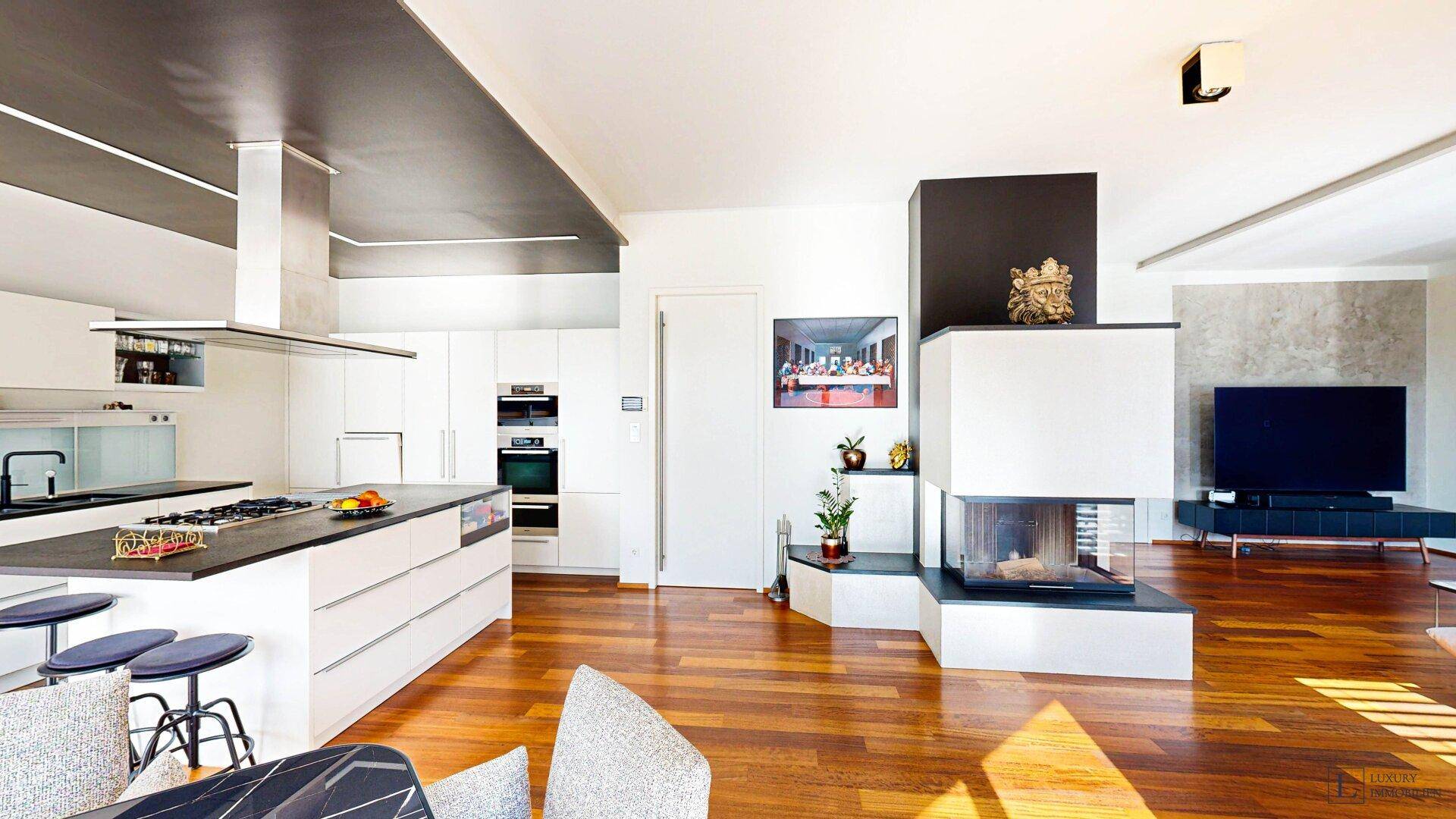 Moderner Wohnbereich mit Kamin, Holzboden und offener Küche im Hintergrund.