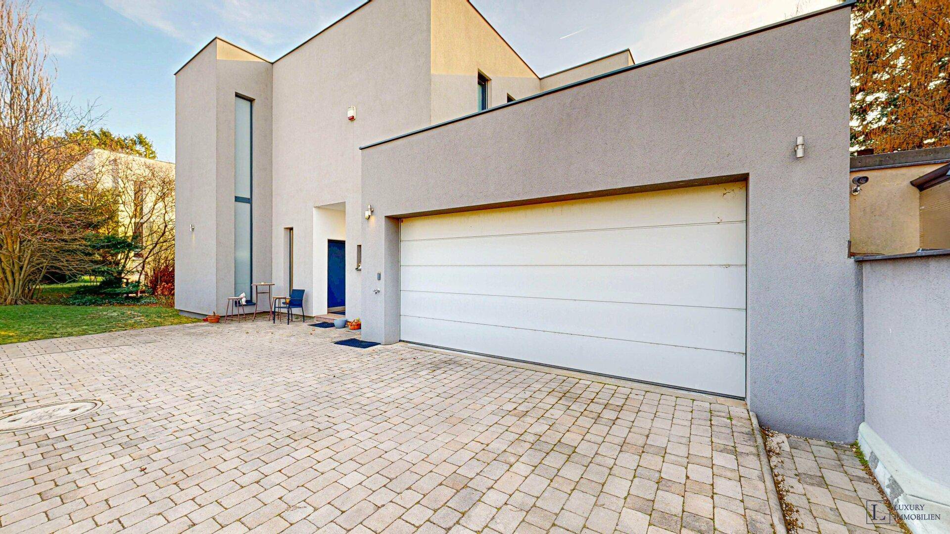 Moderne Hausfassade mit Doppelgarage und gepflasterter Einfahrt.