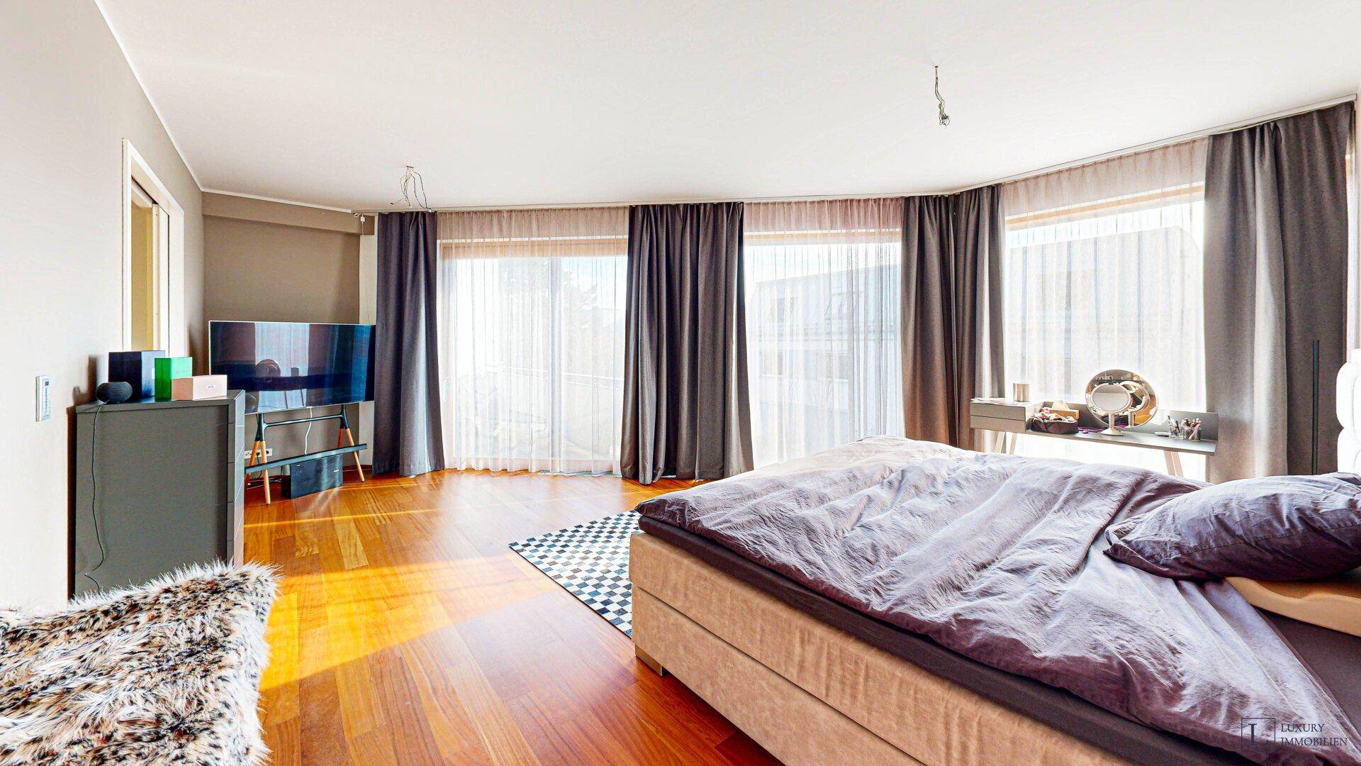Geräumiges Schlafzimmer mit Holzboden, großen Fenstern und viel Tageslicht.