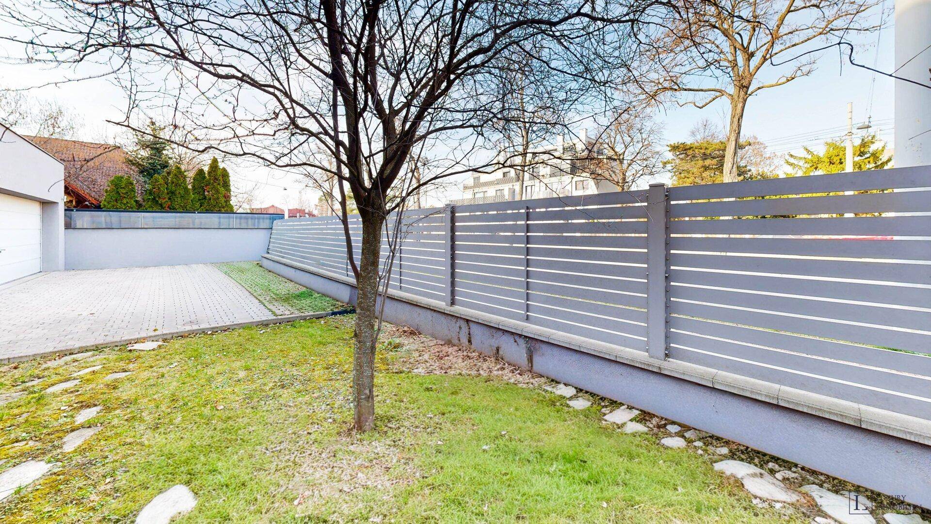 Gartenbereich mit Rasen, modernem Zaun und angrenzender Einfahrt.