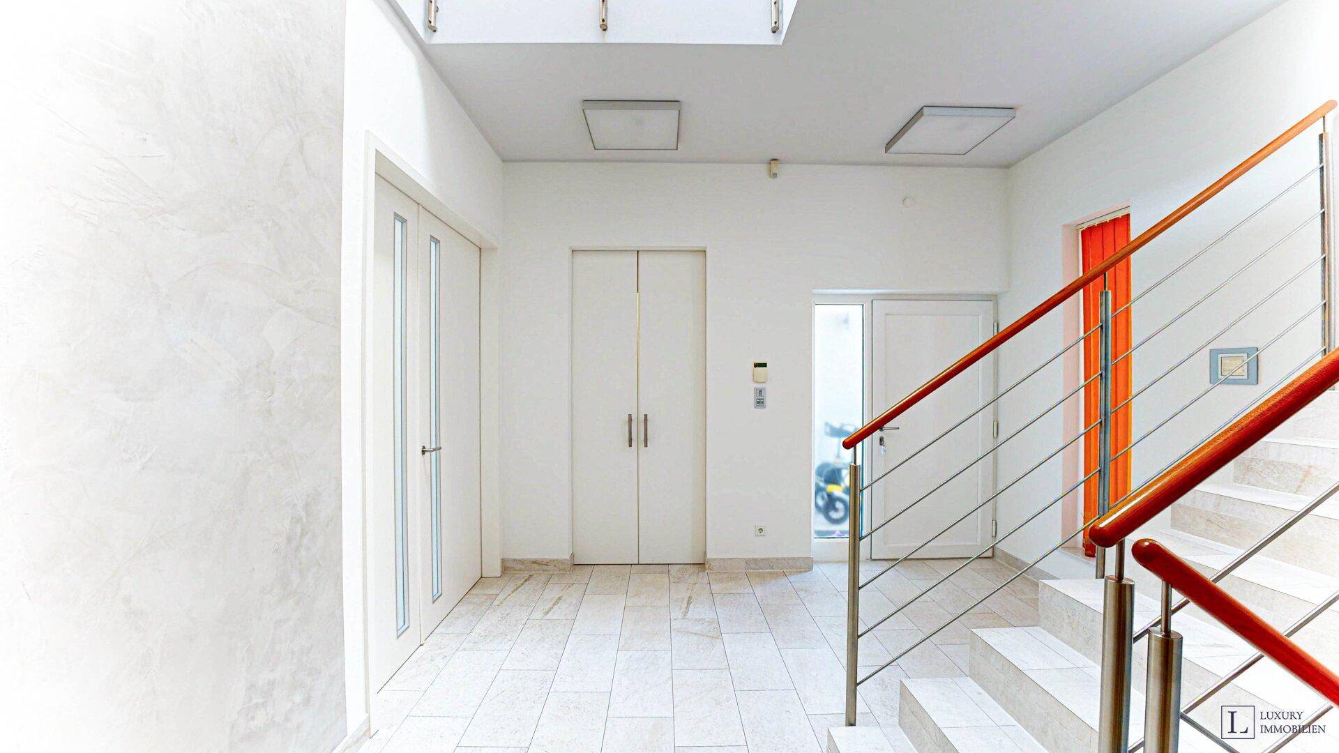 Heller Eingangsbereich mit Treppe, Fliesenboden und Zugang zum Aufzug.