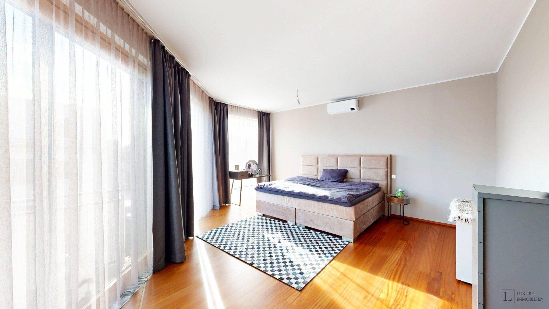Helles Schlafzimmer mit großzügigen Fenstern, Holzboden und Klimaanlage.