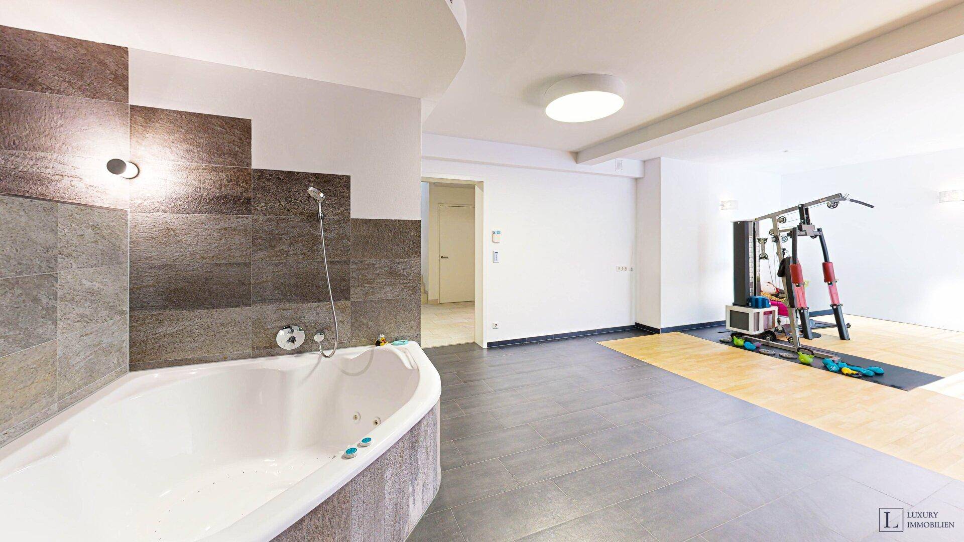 Großzügiger Wellnessbereich mit Whirlpool und Fitnessgeräten.