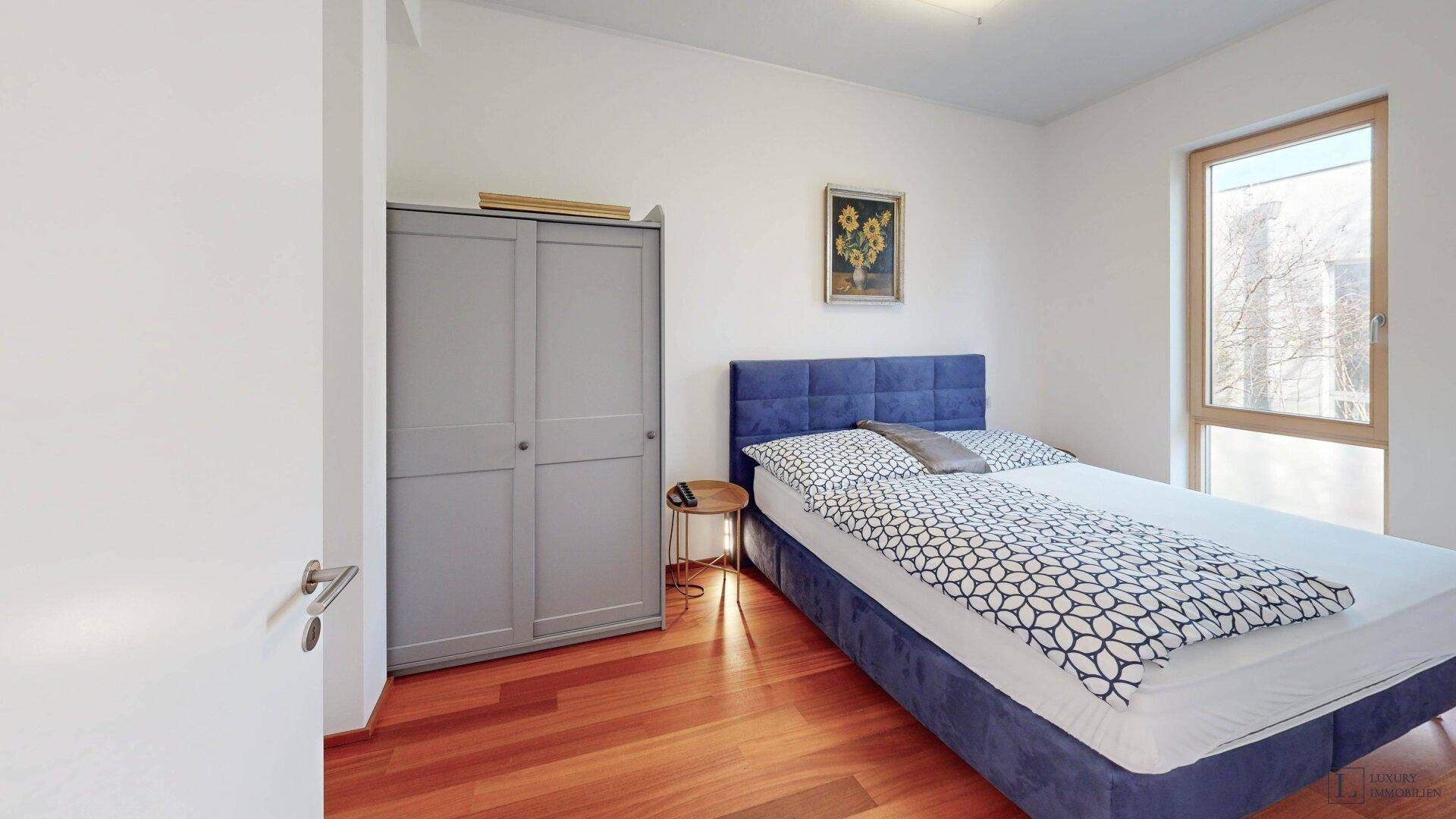 Gemütliches Schlafzimmer mit Holzboden, großem Fenster und Kleiderschrank.
