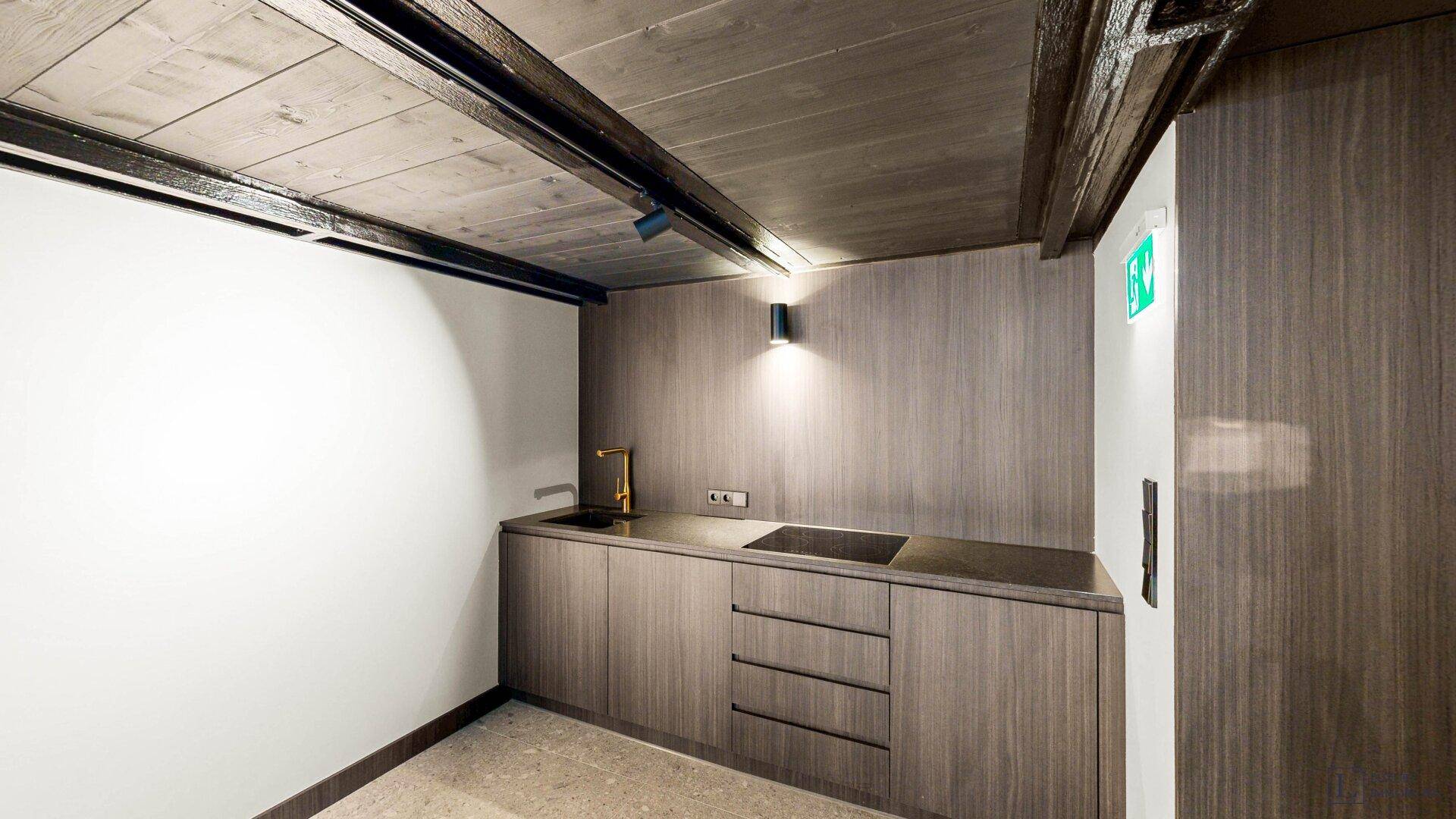 Moderne Küchenzeile mit dunklen Holzschränken, Spüle und goldfarbenen Armaturen in einem Gewerberaum.