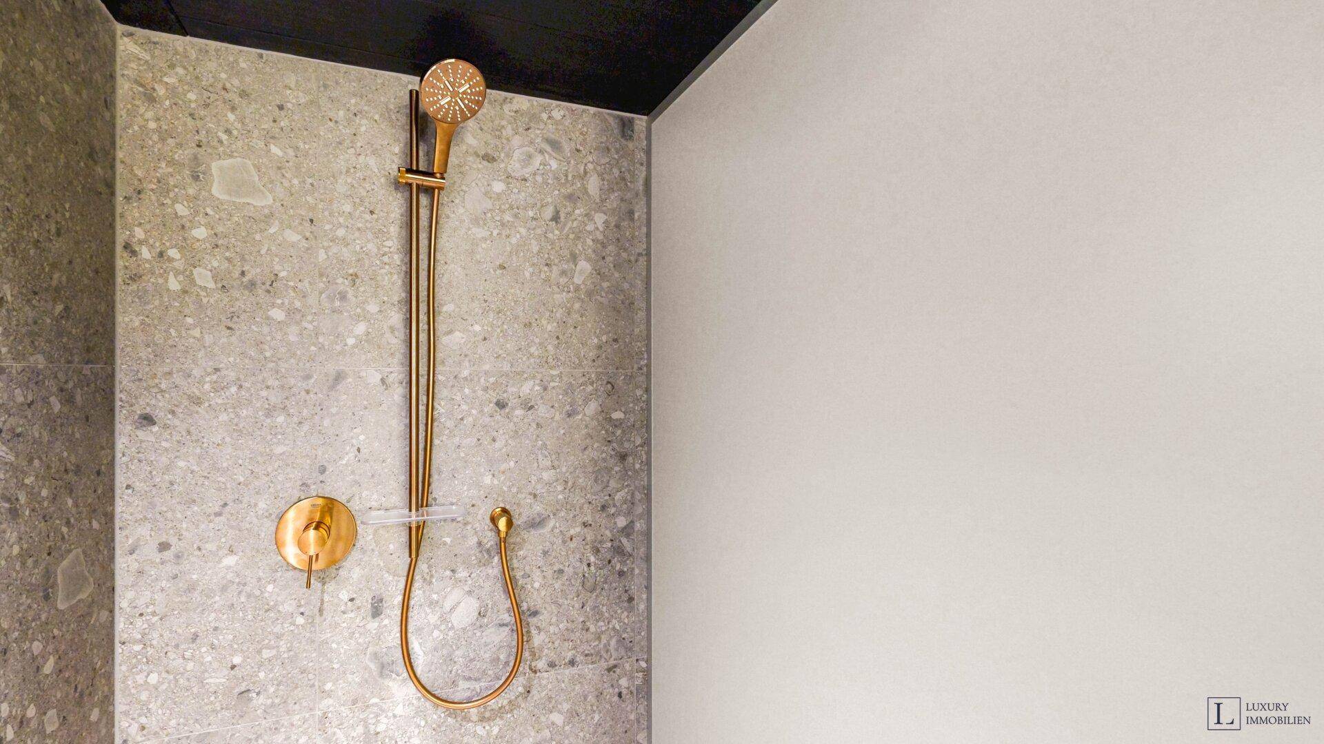 Detailaufnahme einer modernen Duscharmatur in Gold an einer gefliesten Wand.