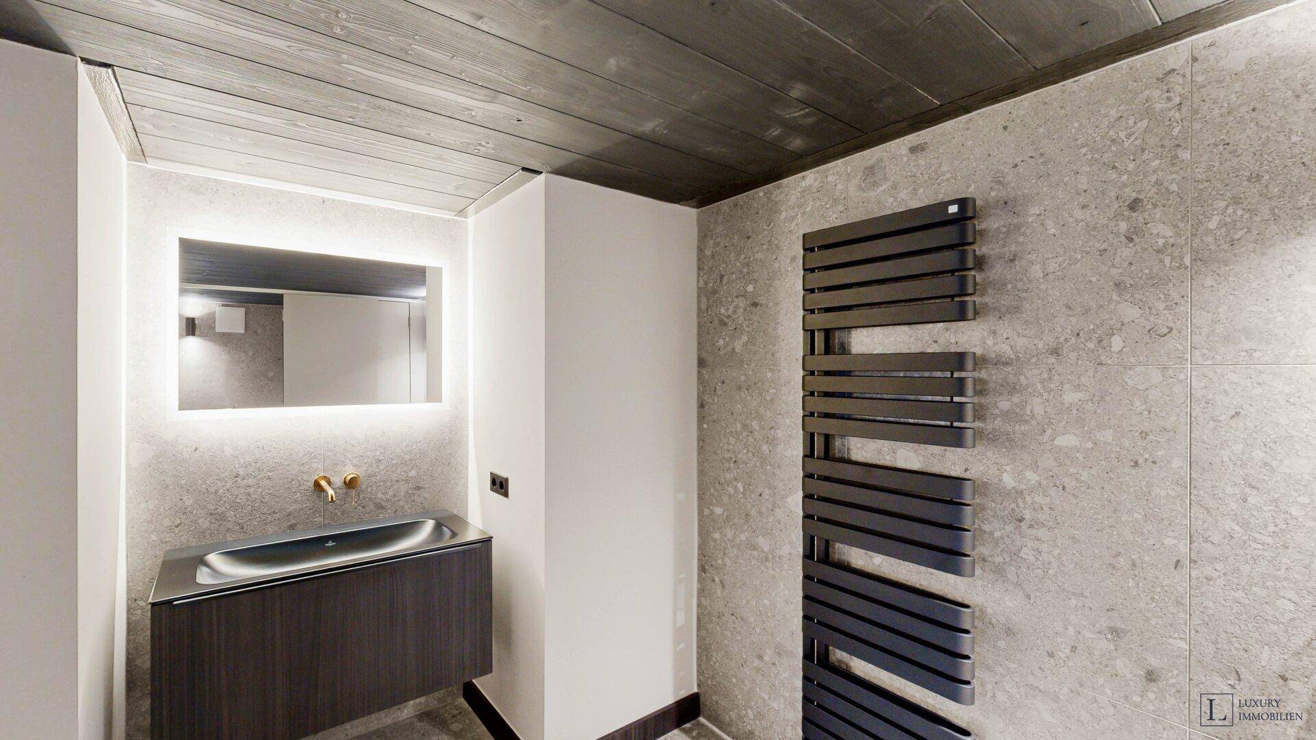 Modernes Badezimmer mit Waschtisch, beleuchtetem Spiegel und Handtuchheizkörper.