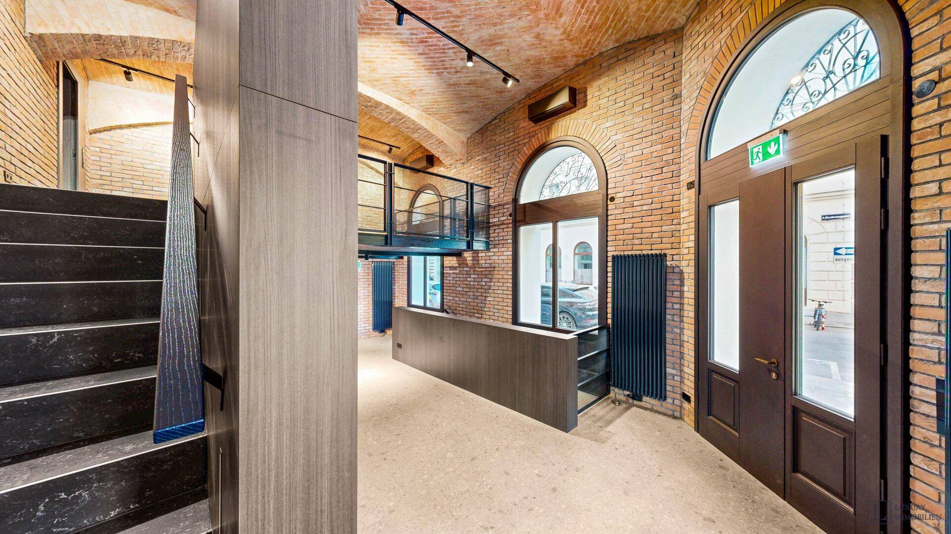 Eingangsbereich eines Gewerberaums mit Treppe, Ziegelwänden und Blick auf die Galerie.