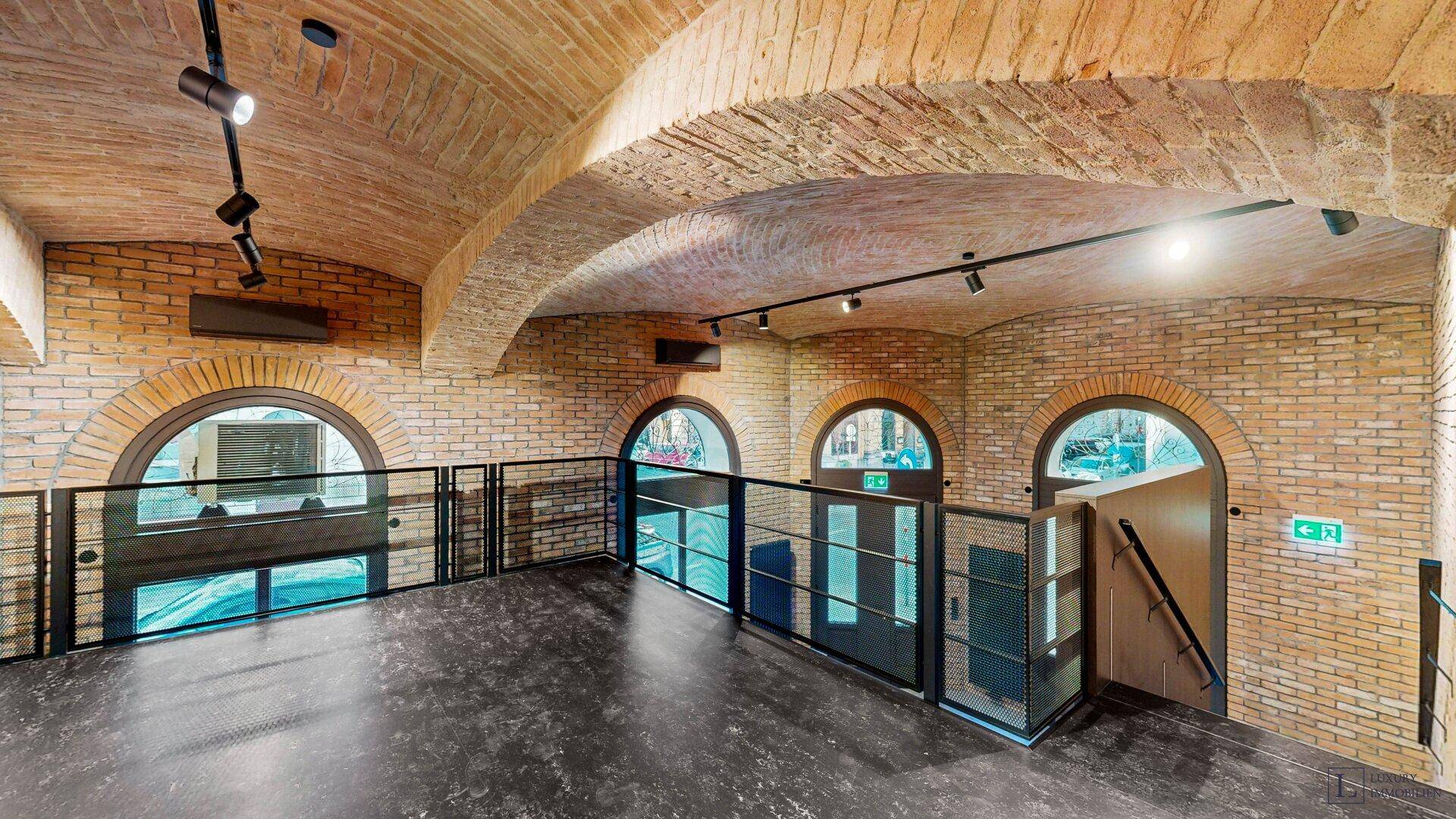Helle Galerieebene mit mehreren Rundbogenfenstern, Ziegelgewölbedecke und moderner Beleuchtung.