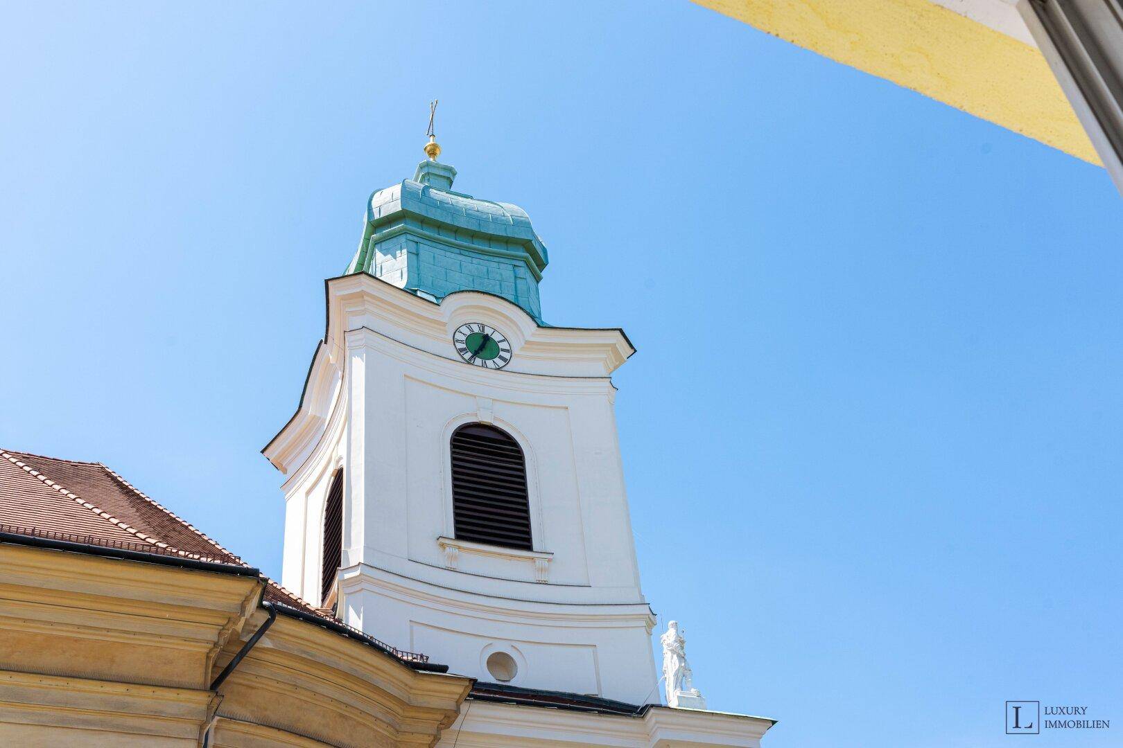 Historischer Kirchturm mit Uhr und grünem Kupferdach unter strahlend blauem Himmel.