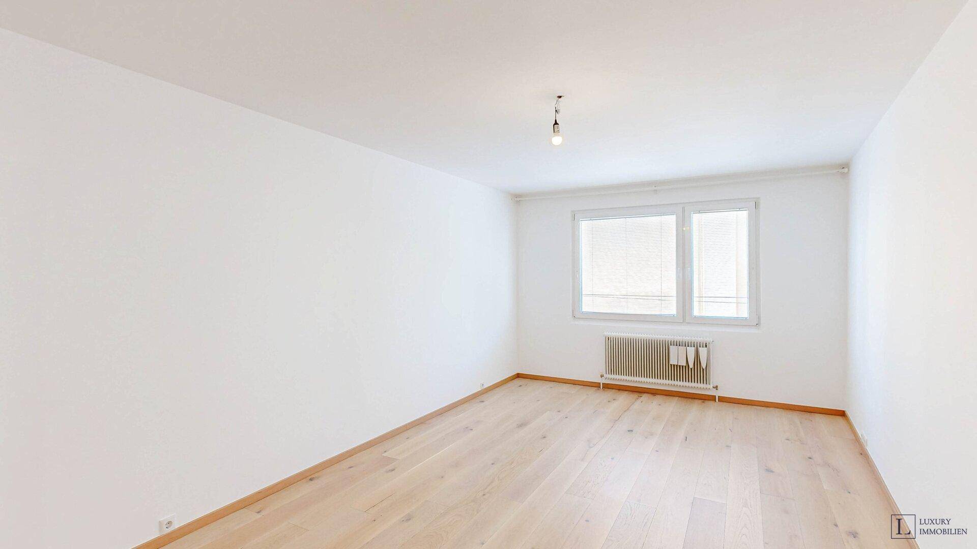 Helles, unmöbliertes Zimmer mit Holzfußboden und Fenster, das viel Tageslicht hereinlässt.