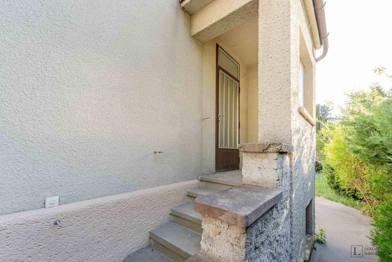 Eingangsbereich des Hauses mit Steinstufen und einer einfachen braunen Haustür.