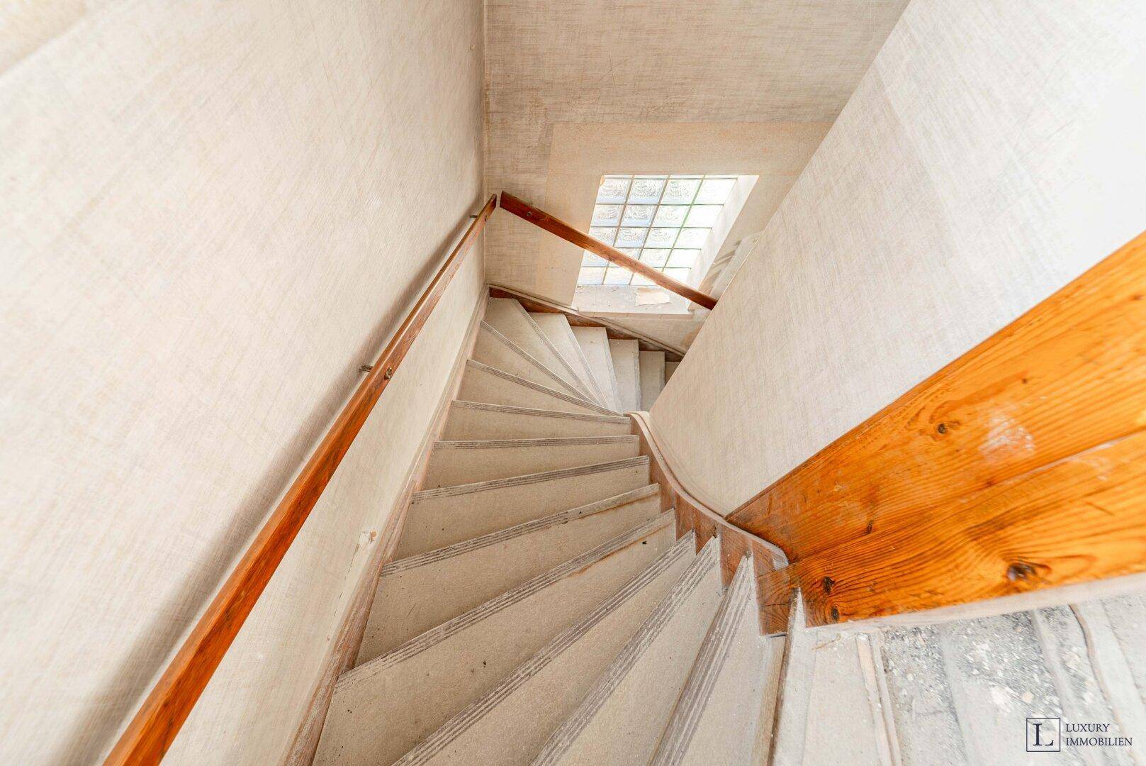 Wendeltreppe mit Holzgeländer und einem Glasbausteinfenster, das Licht spendet.