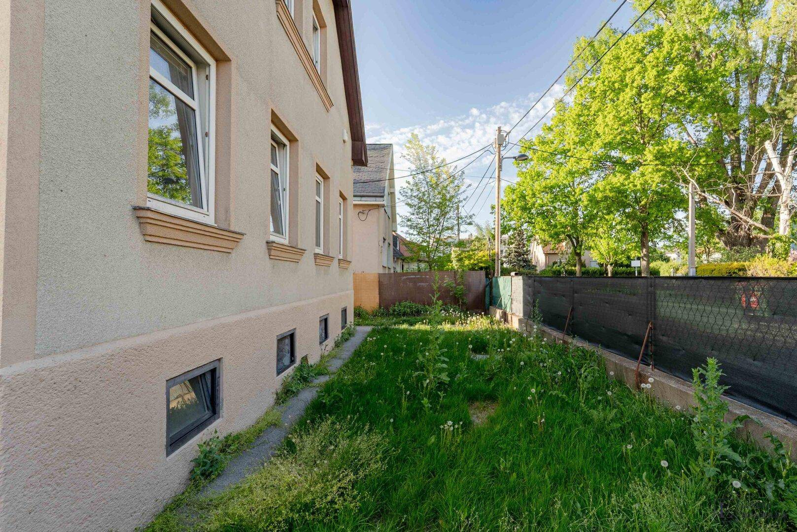 Seitenansicht des Hauses mit schmalem Gartenstreifen und kleinen Kellerfenstern.