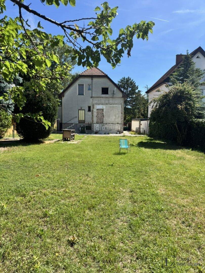 Hinteransicht des Hauses mit großem Rasenbereich und Bäumen im Garten.