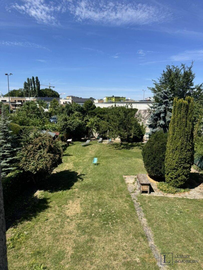 Weitläufiger Gartenbereich mit Rasenfläche und altem Baumbestand, umgeben von weiterer Bebauung.