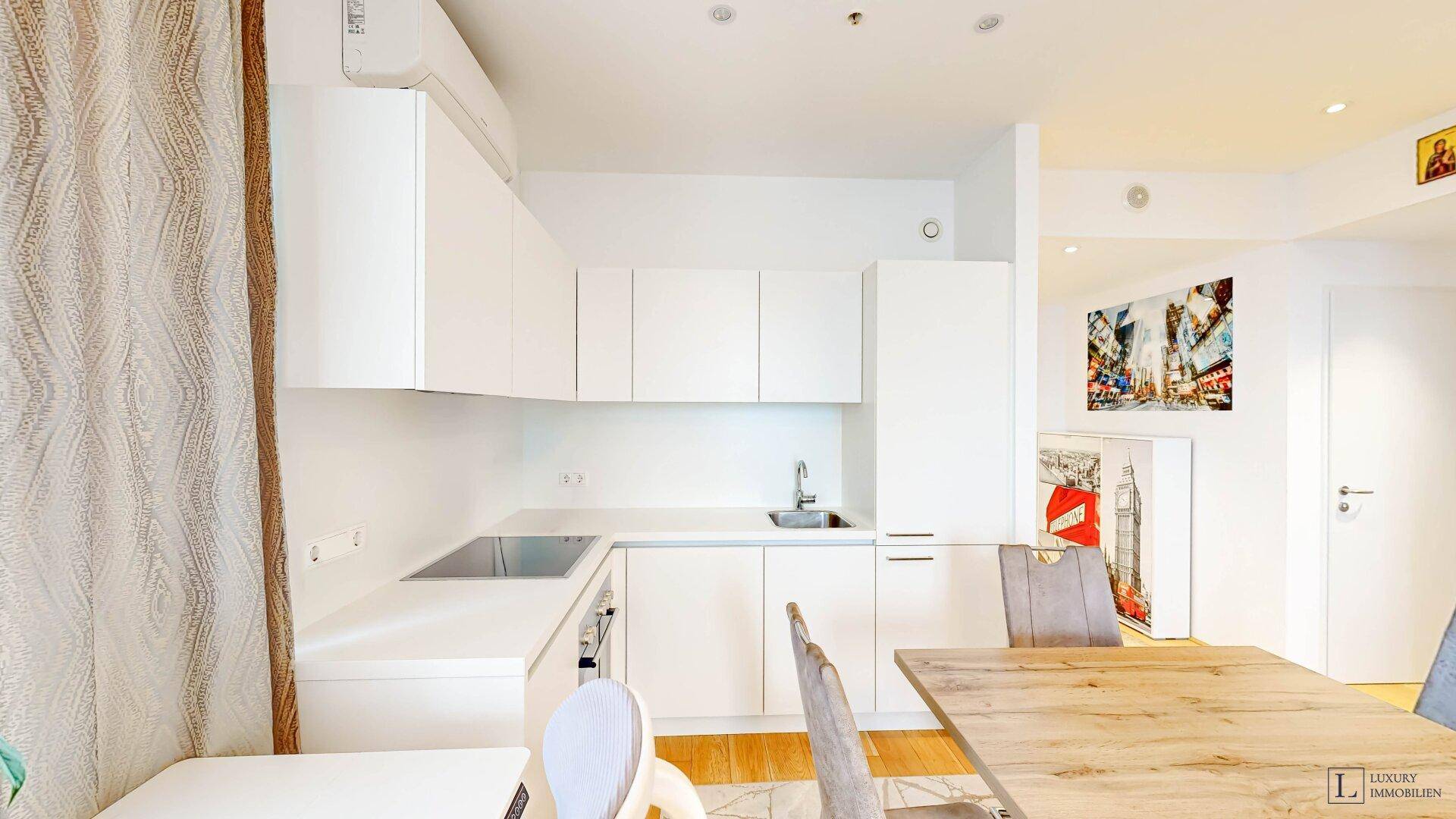 Moderne weiße Einbauküche mit Induktionskochfeld und integriertem Backofen im offenen Wohnbereich.