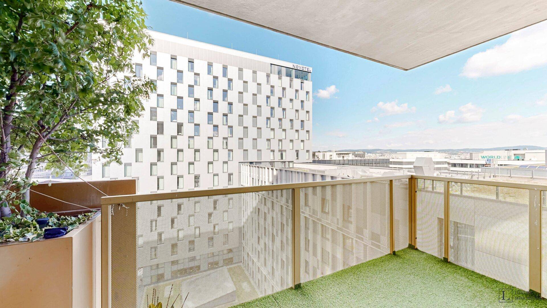 Balkon mit Kunstrasen und Stadtblick auf umliegende Gebäude und Bahngleise.