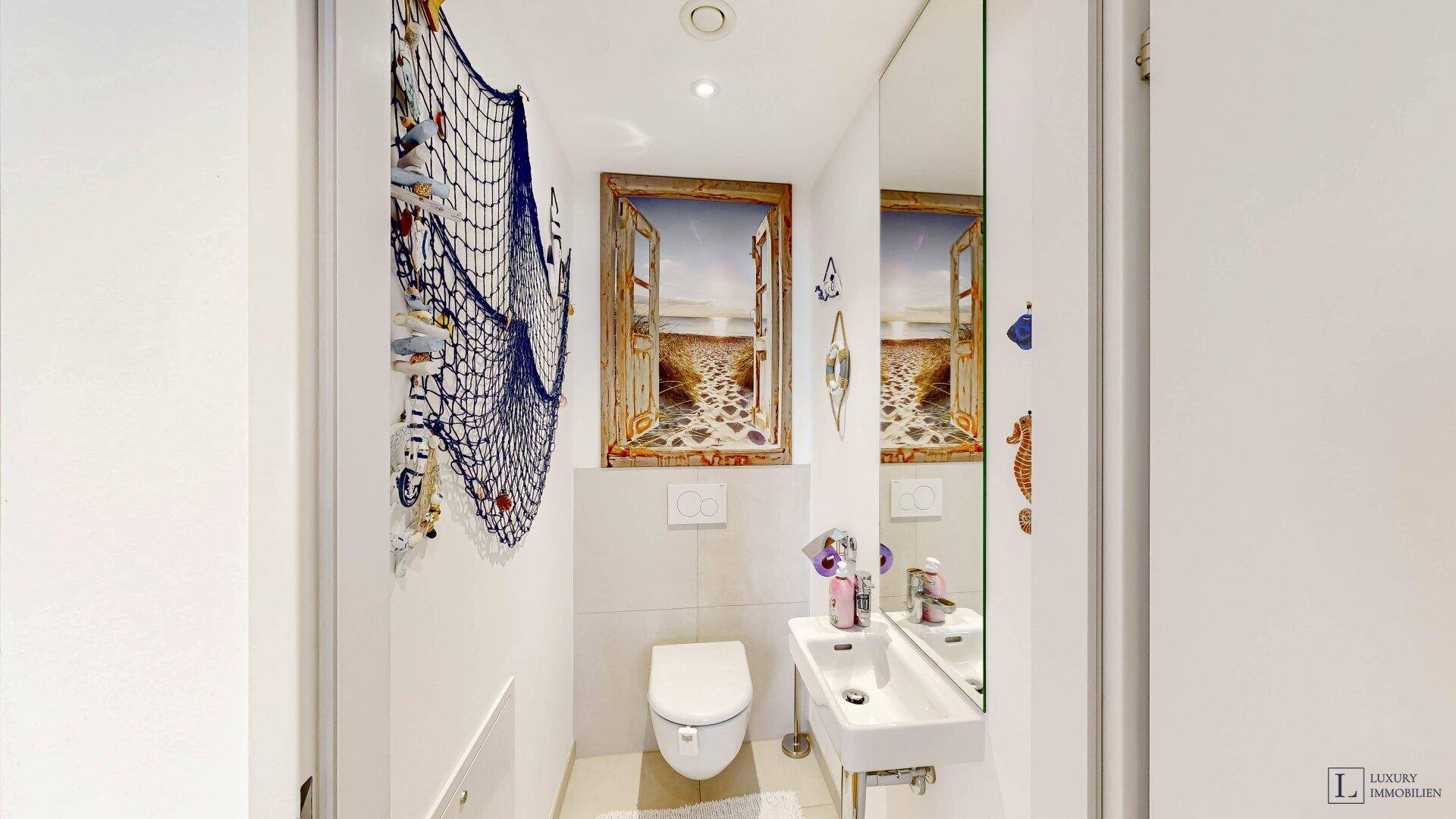 Separates WC mit wandhängender Toilette, kleinem Waschbecken und maritimer Dekoration.