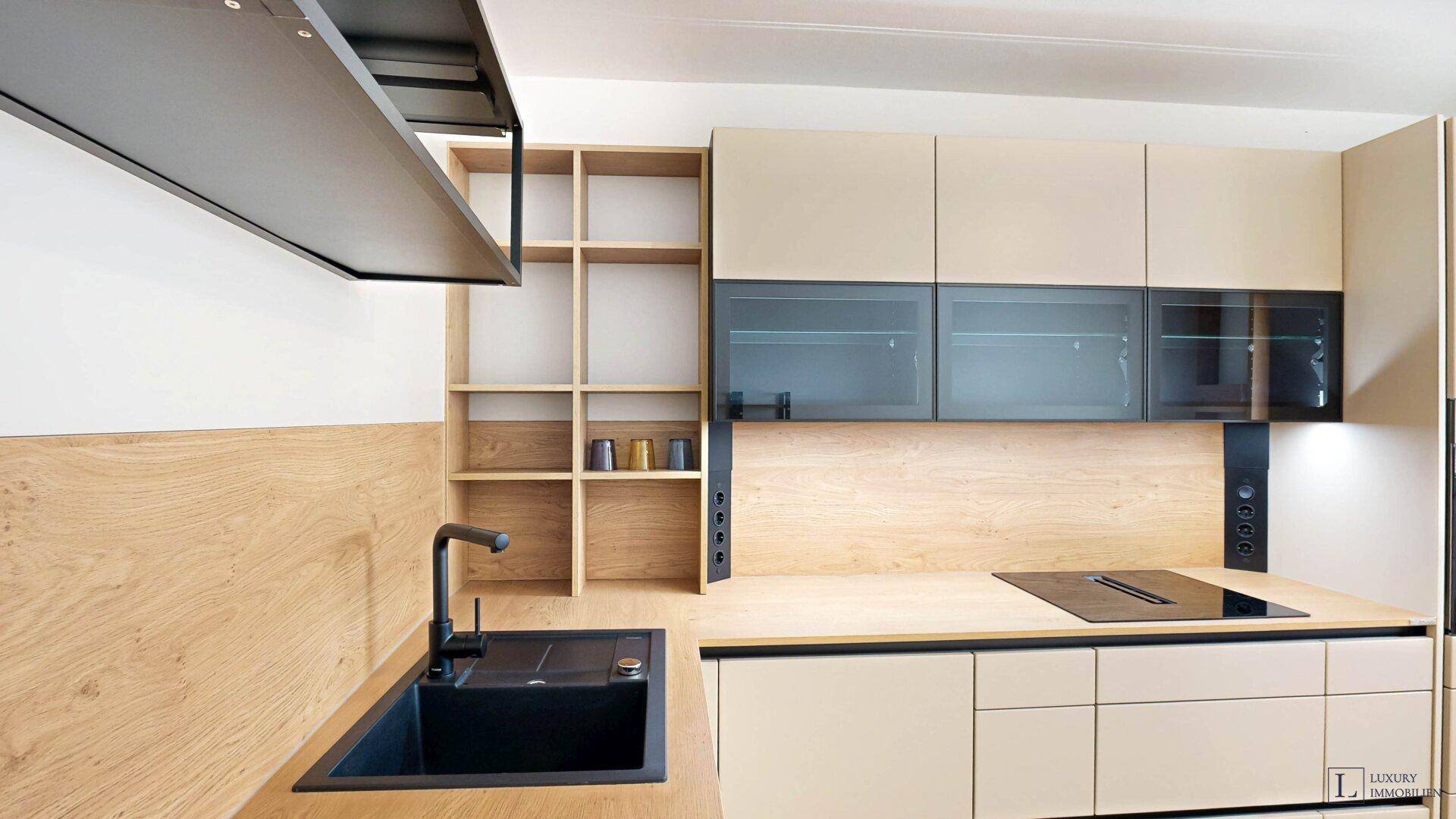 Moderne Einbauküche mit hellen Holzfronten, beigen Schränken, schwarzer Spüle und integriertem Induktionskochfeld.