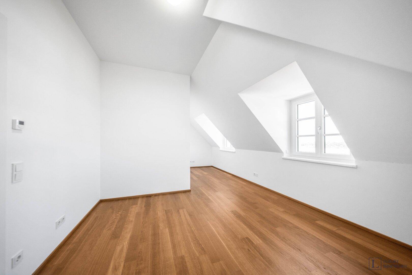 Heller Raum mit Holzboden, Dachschrägen und mehreren Fenstern für viel Tageslicht.