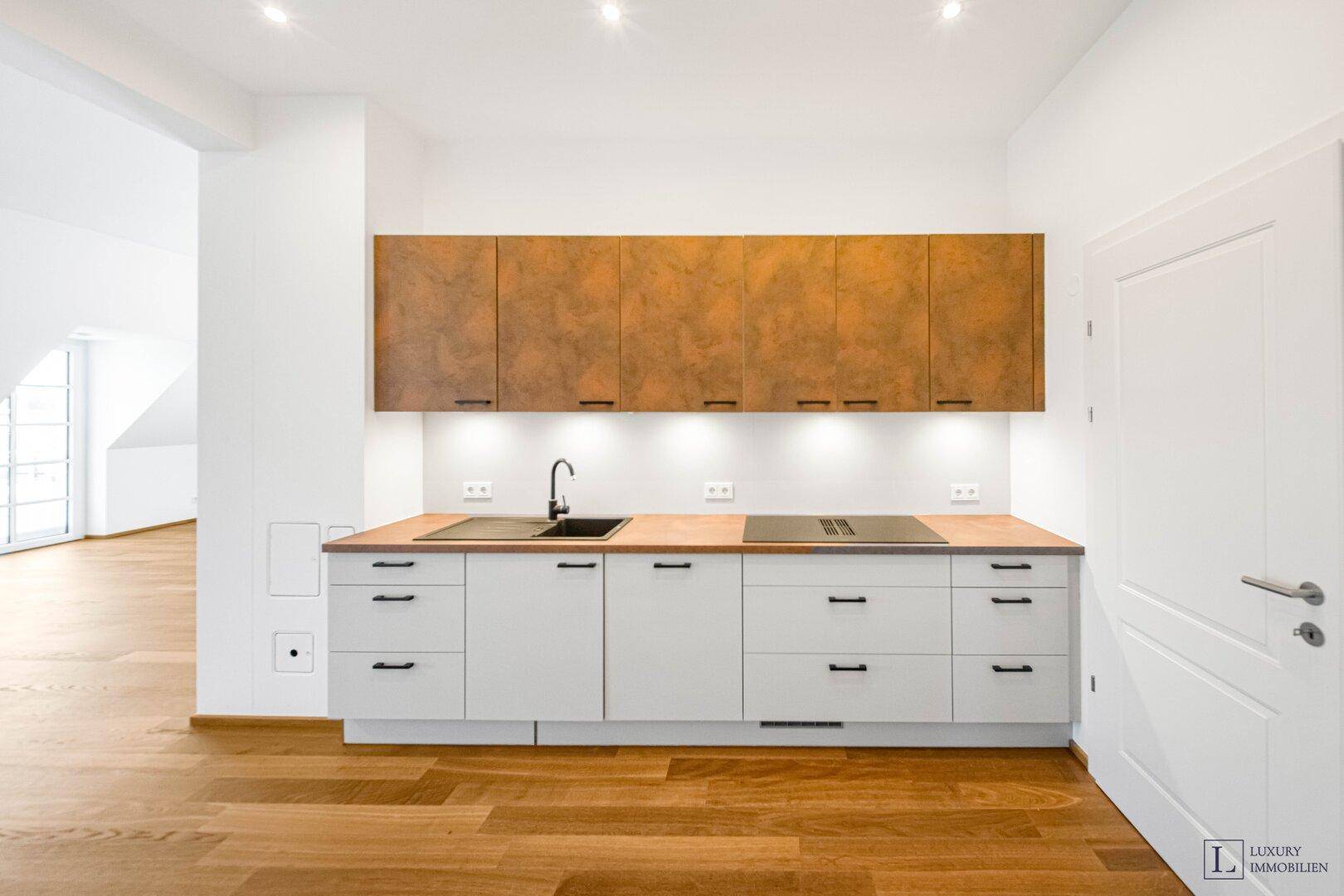 Moderne Einbauküche mit weißen Unterschränken, Holz-Arbeitsplatte und braunen Oberschränken.