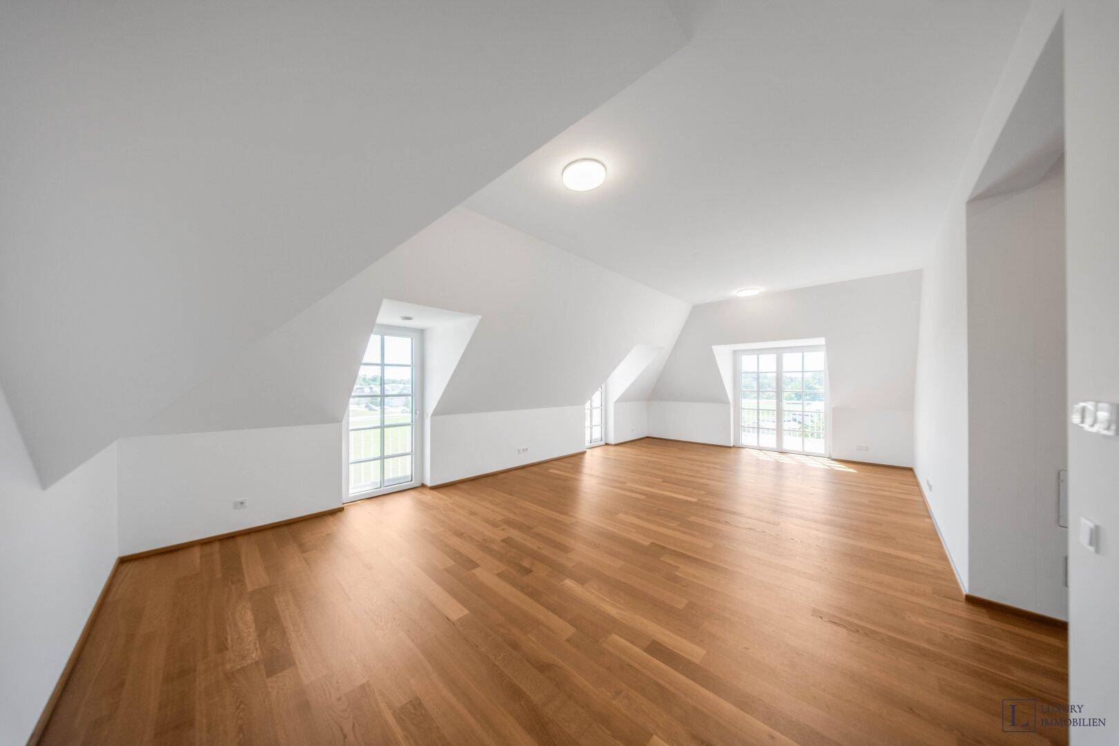 Geräumiger, heller Raum mit Holzboden, Dachschrägen und mehreren Fenstern.