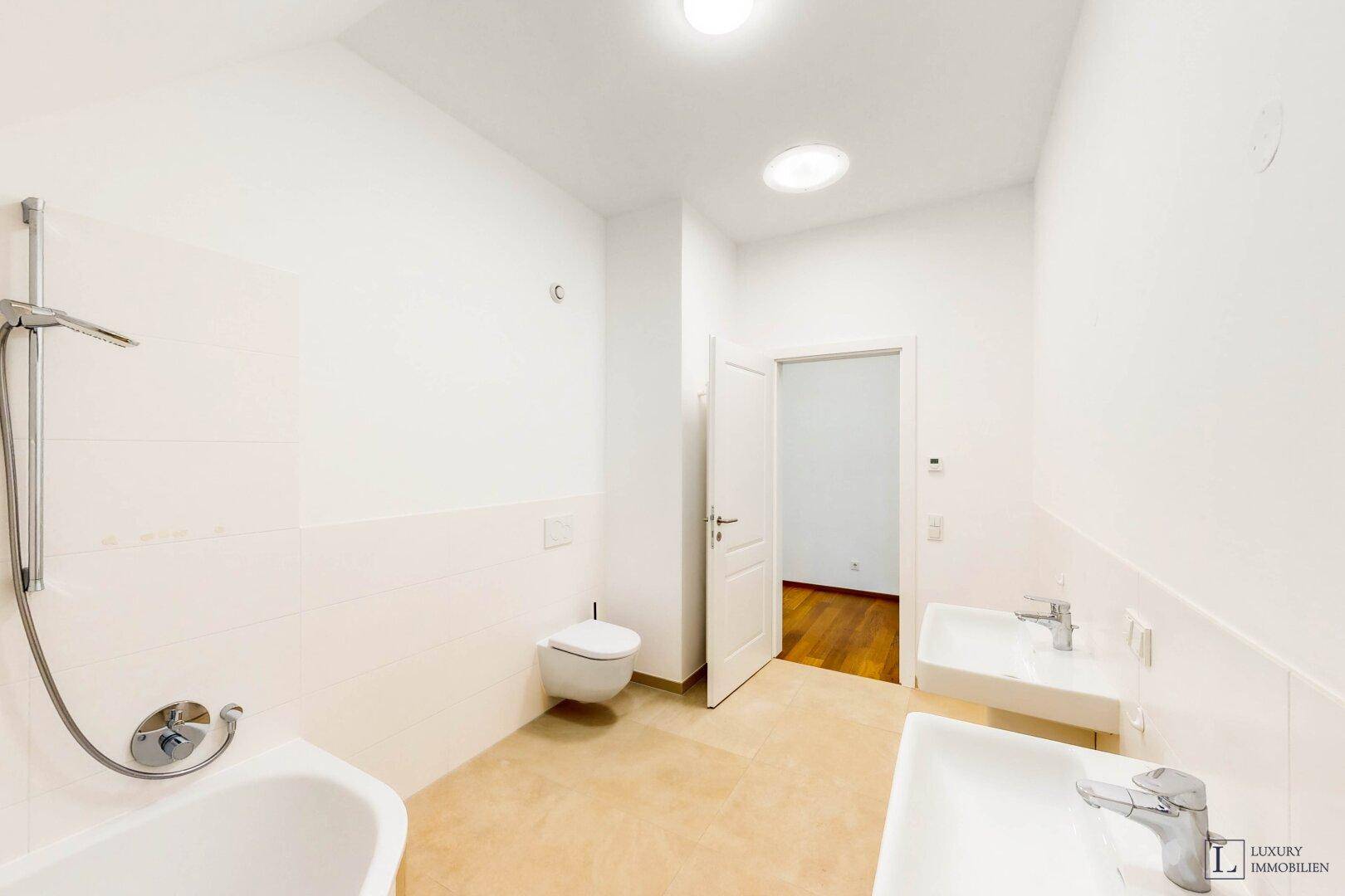 Modernes Badezimmer mit Doppelwaschbecken, Badewanne mit Duschfunktion und hellen Fliesen.