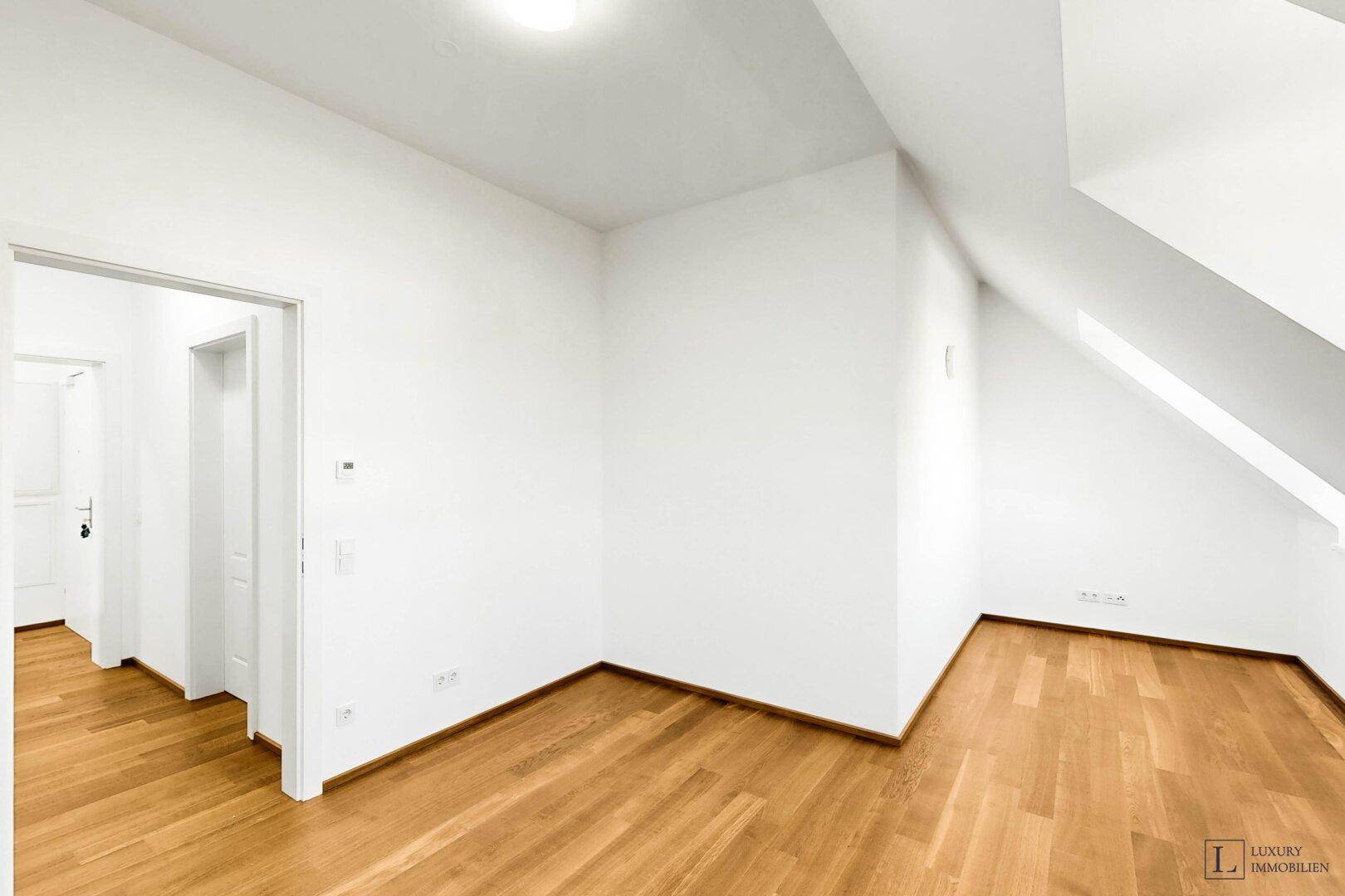 Heller Raum mit Holzboden, weißen Wänden und Zugang zu einem weiteren Bereich.